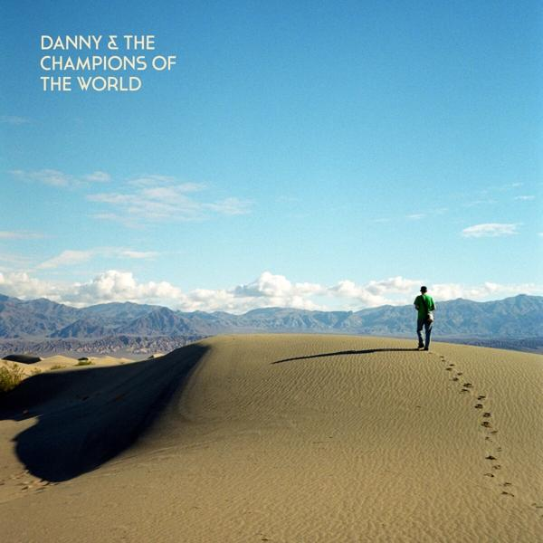 Albumcover: Ein Mann geht auf einer Sanddüne, blauer Himmel und Bergkette im Hintergrund.