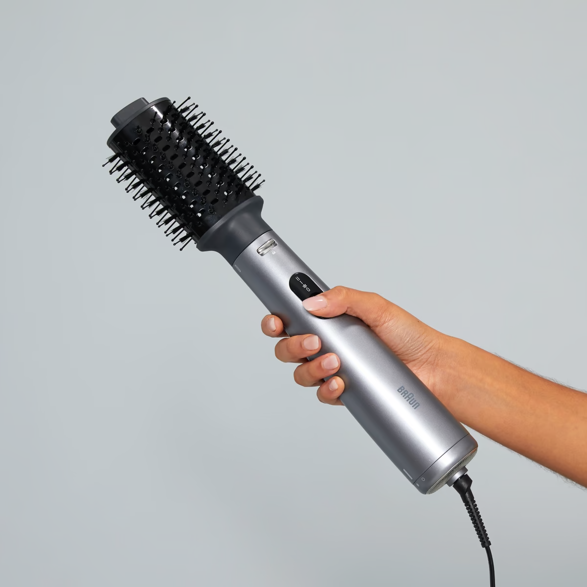 La main d'une personne tient un outil de coiffure gris et noir.