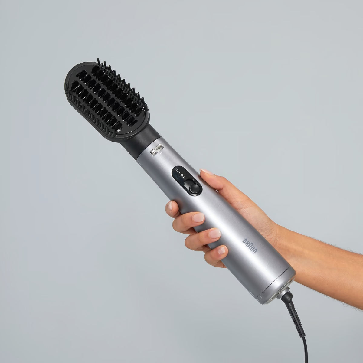 Un styler capillaire Braun argenté tenu par une personne avec un arrière-plan neutre.
