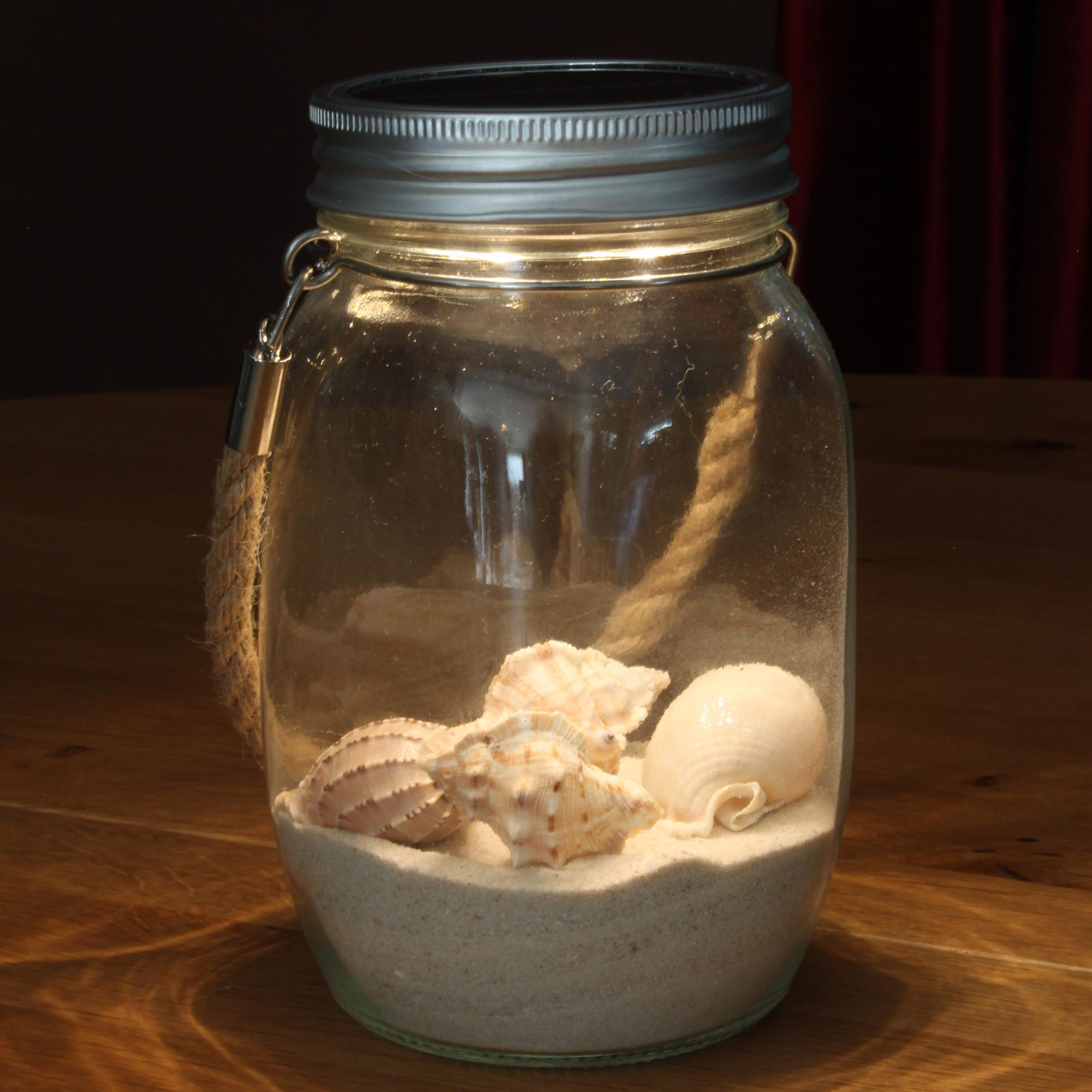 Glasbehälter mit Sand, Muscheln und Metalldeckel, auf Holz.