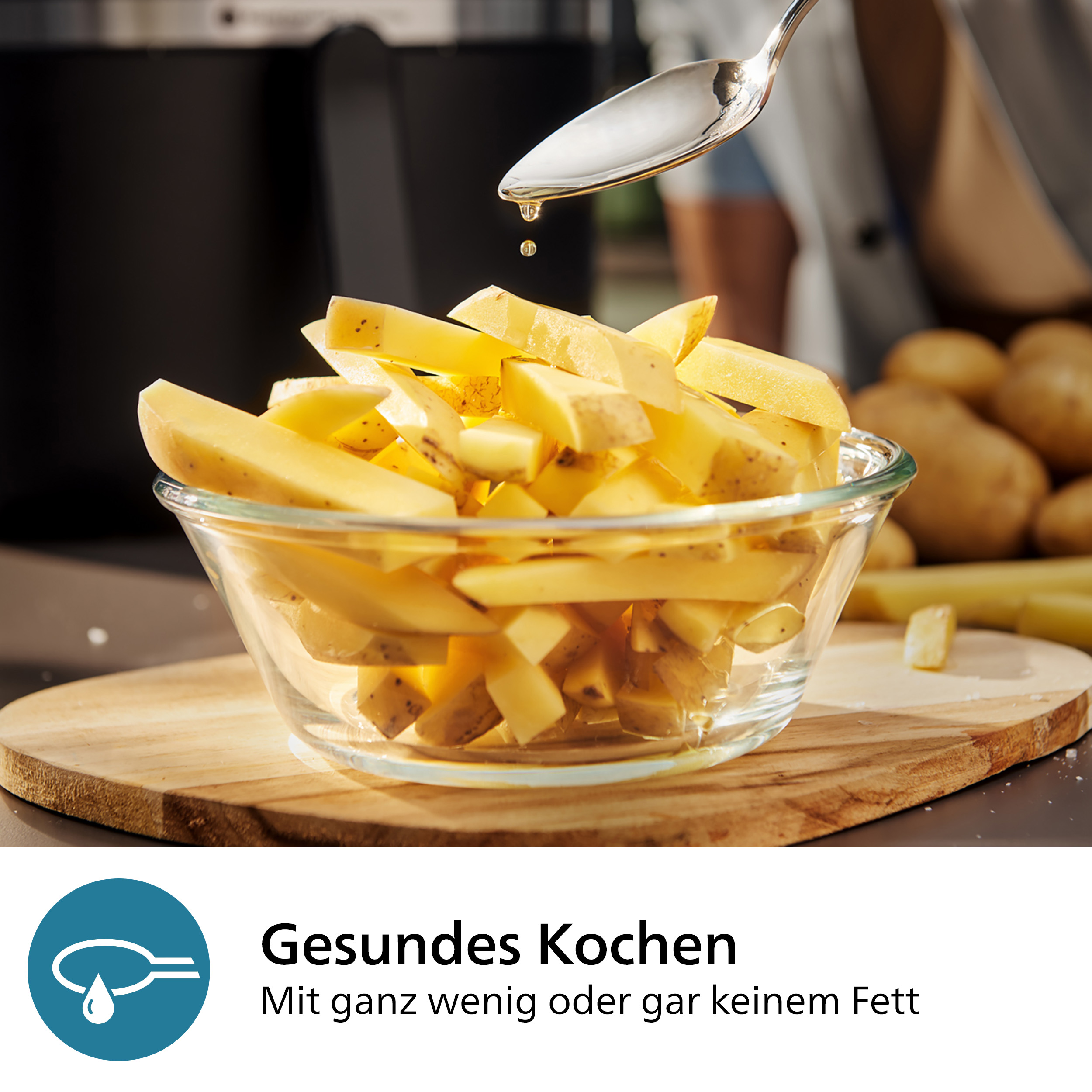 Geschnittene Kartoffeln in Glasschüssel, Öl tropft aus Löffel auf Holzbrett.