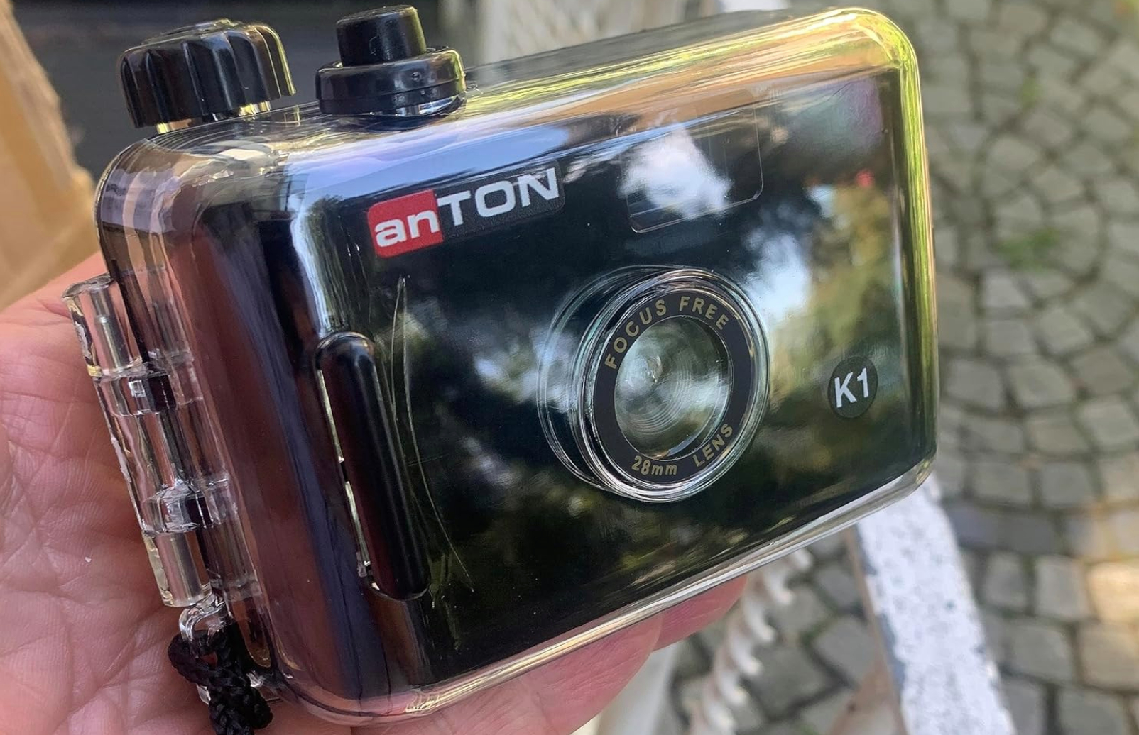 Eine klare, schwarze Anton K1 wasserdichte Kamera in der Hand, mit Objektiv.