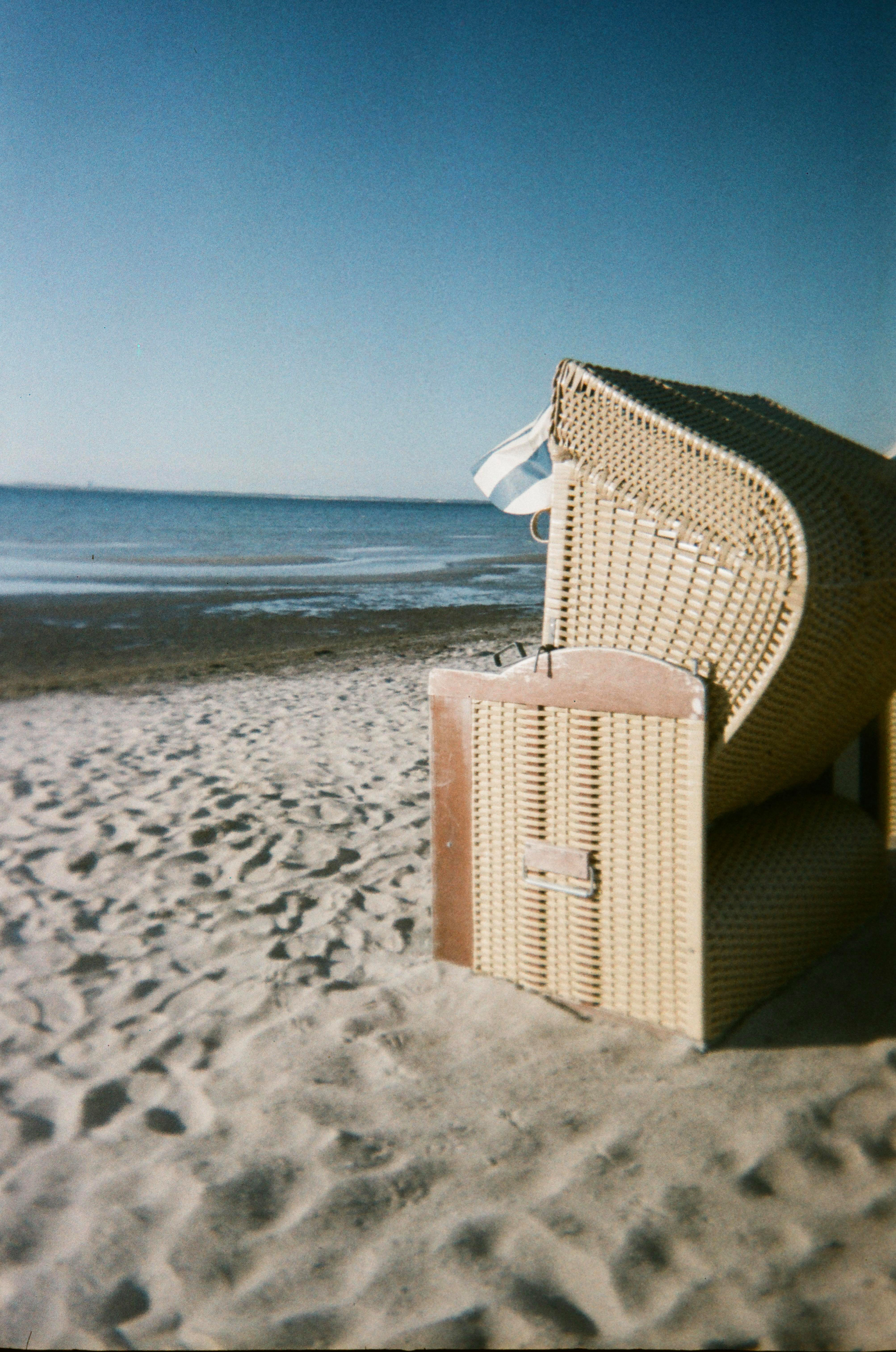 Strandszene mit einem Strandkorb auf Sandstrand, mit Meer und Himmel im Hintergrund.