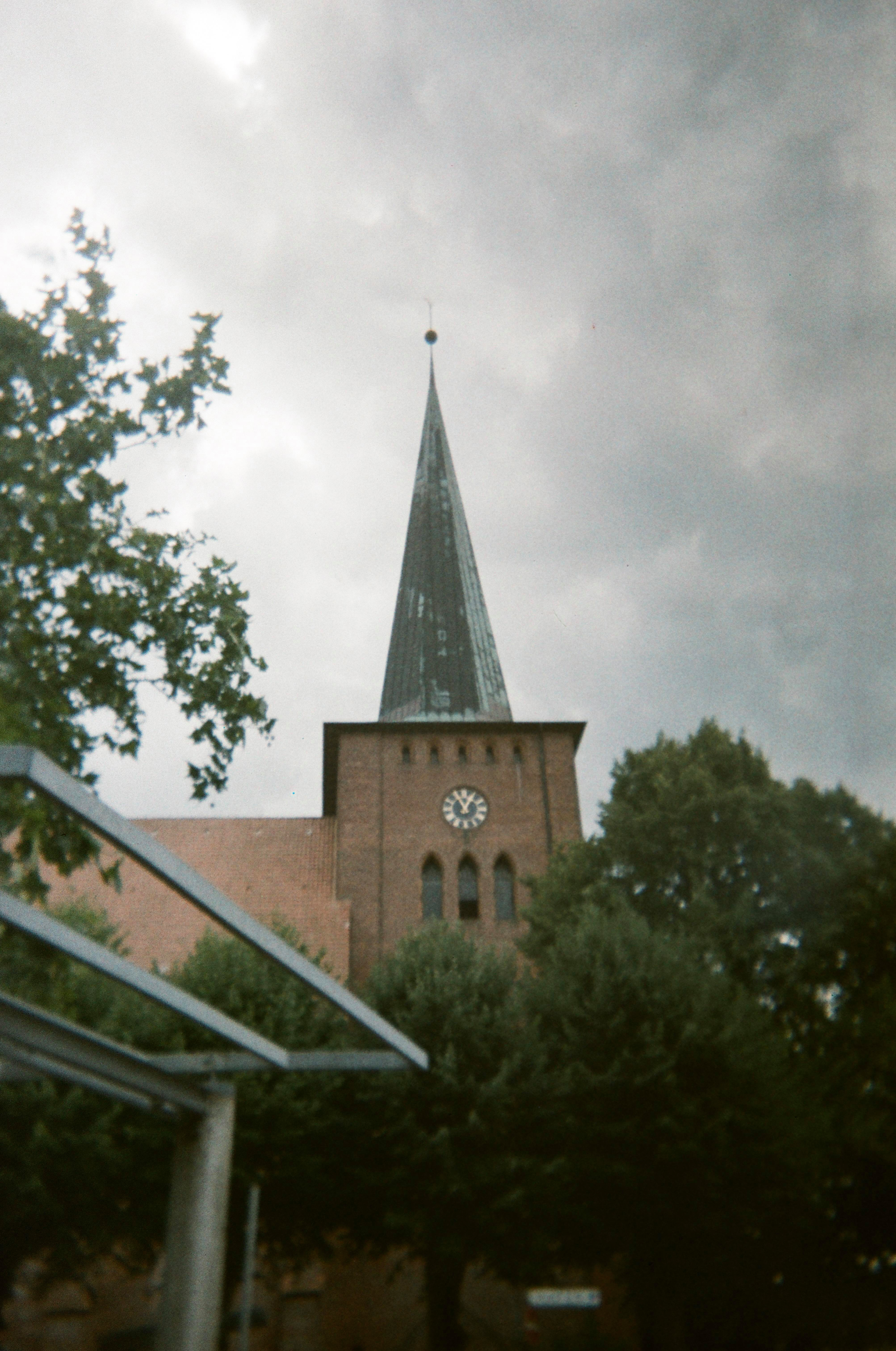 Kirche mit hohem Turm und Uhr unter bewölktem Himmel.