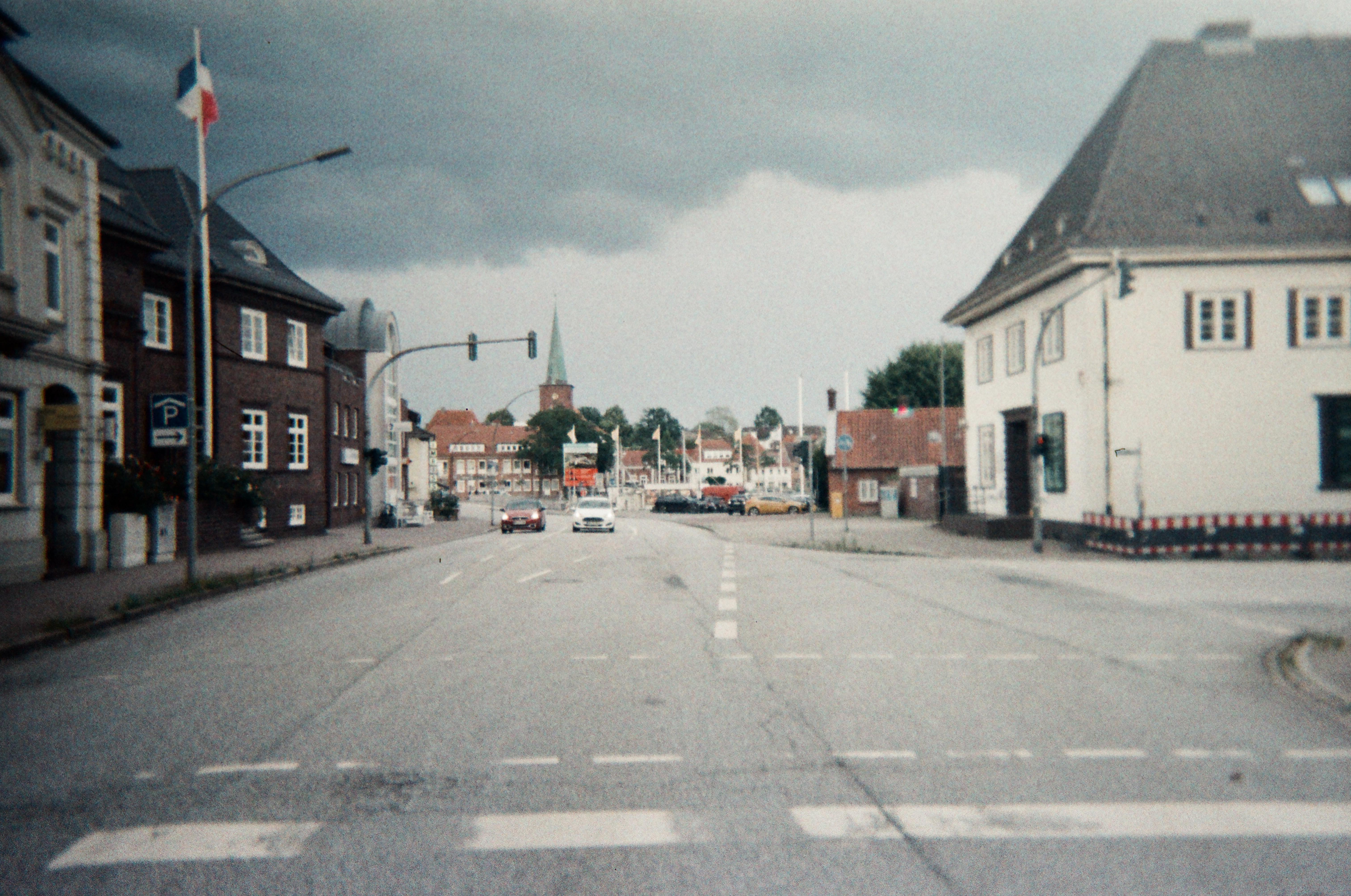 Straßenszene mit Gebäuden auf beiden Seiten, Autos auf der Straße und bewölktem Himmel.