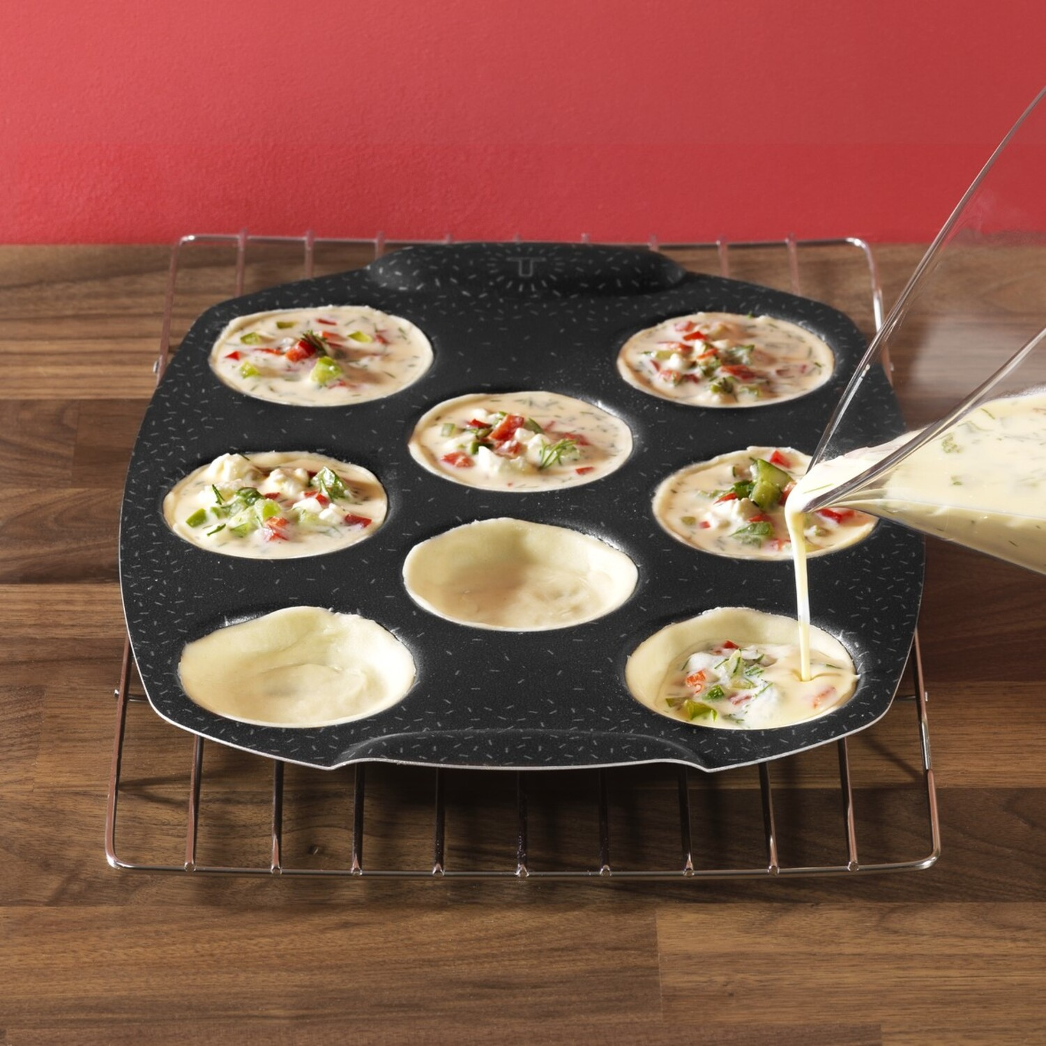 Moule à muffins avec cavités remplies, remplies de pâte ; fond rouge, table en bois.