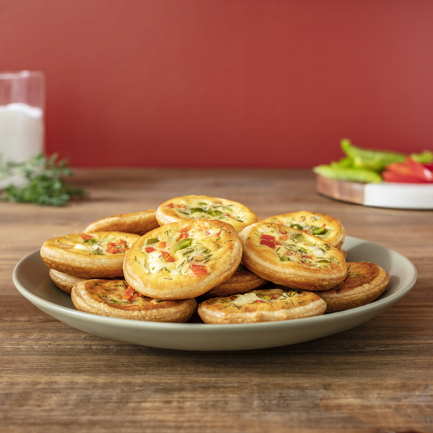 Une assiette de mini quiches aux légumes, à côté d'un verre de lait et un fond rouge.