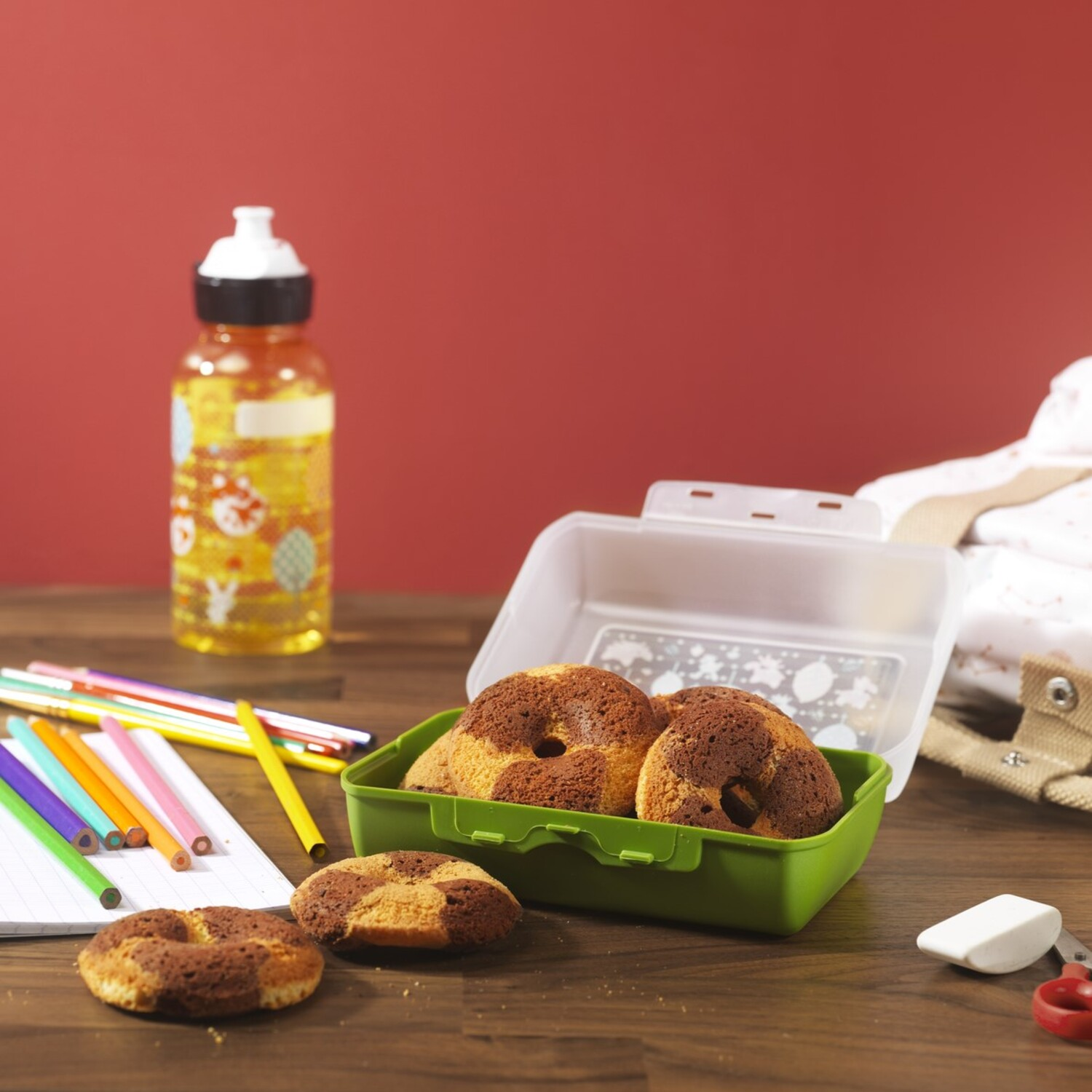 Lunch box with donuts, pencils, and a water bottle on a table.
