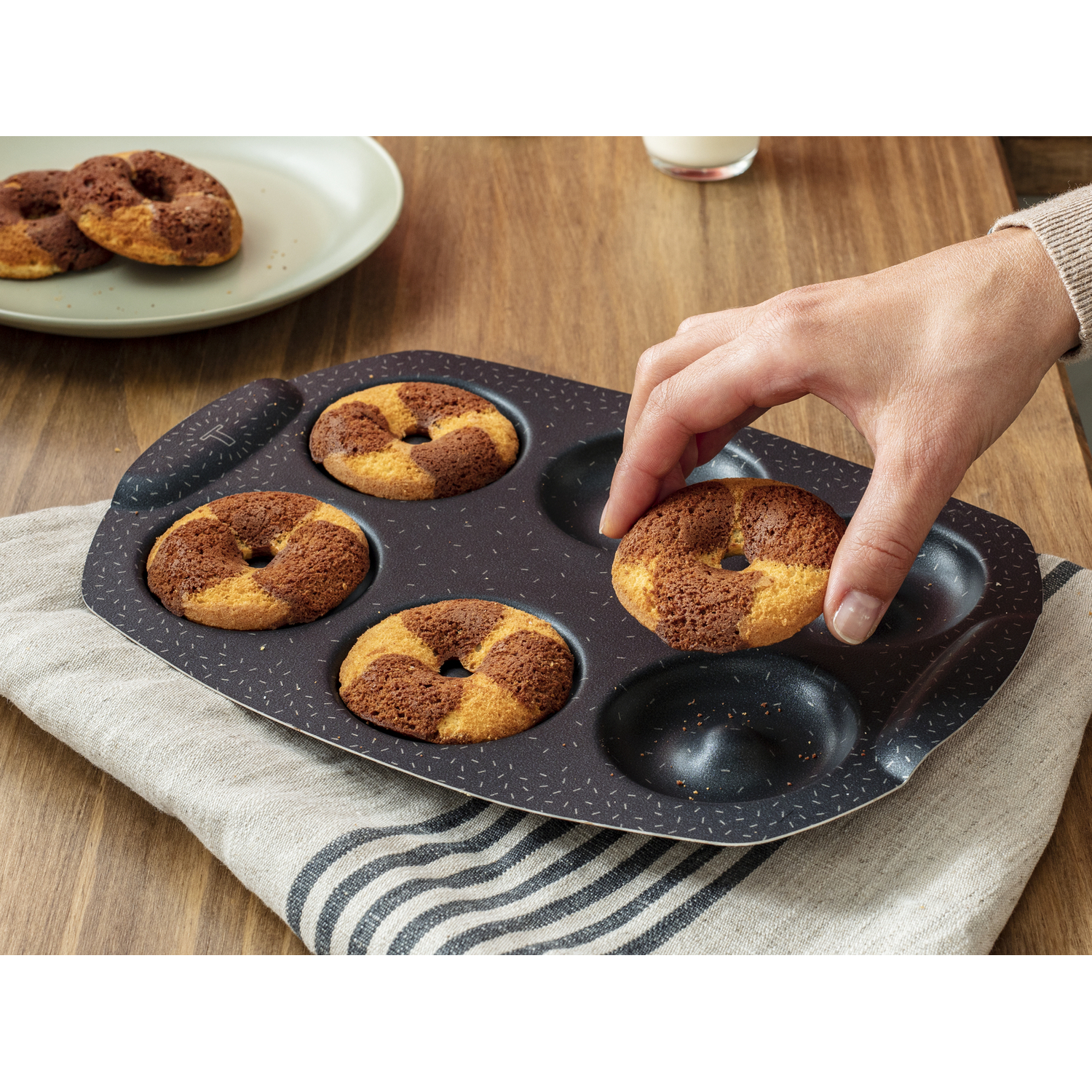 A person's hand taking a muffin from a tray with four muffins. The muffins are brown and yellow.