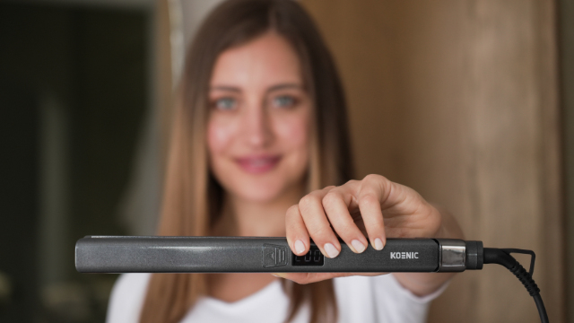Woman holding a gray flat iron, with the brand name KOENIC visible.