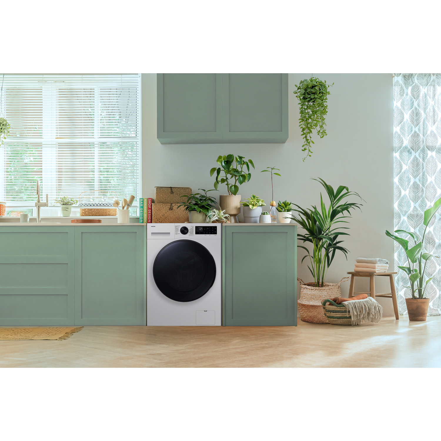 Een witte wasmachine in een groene keuken, omringd door planten.