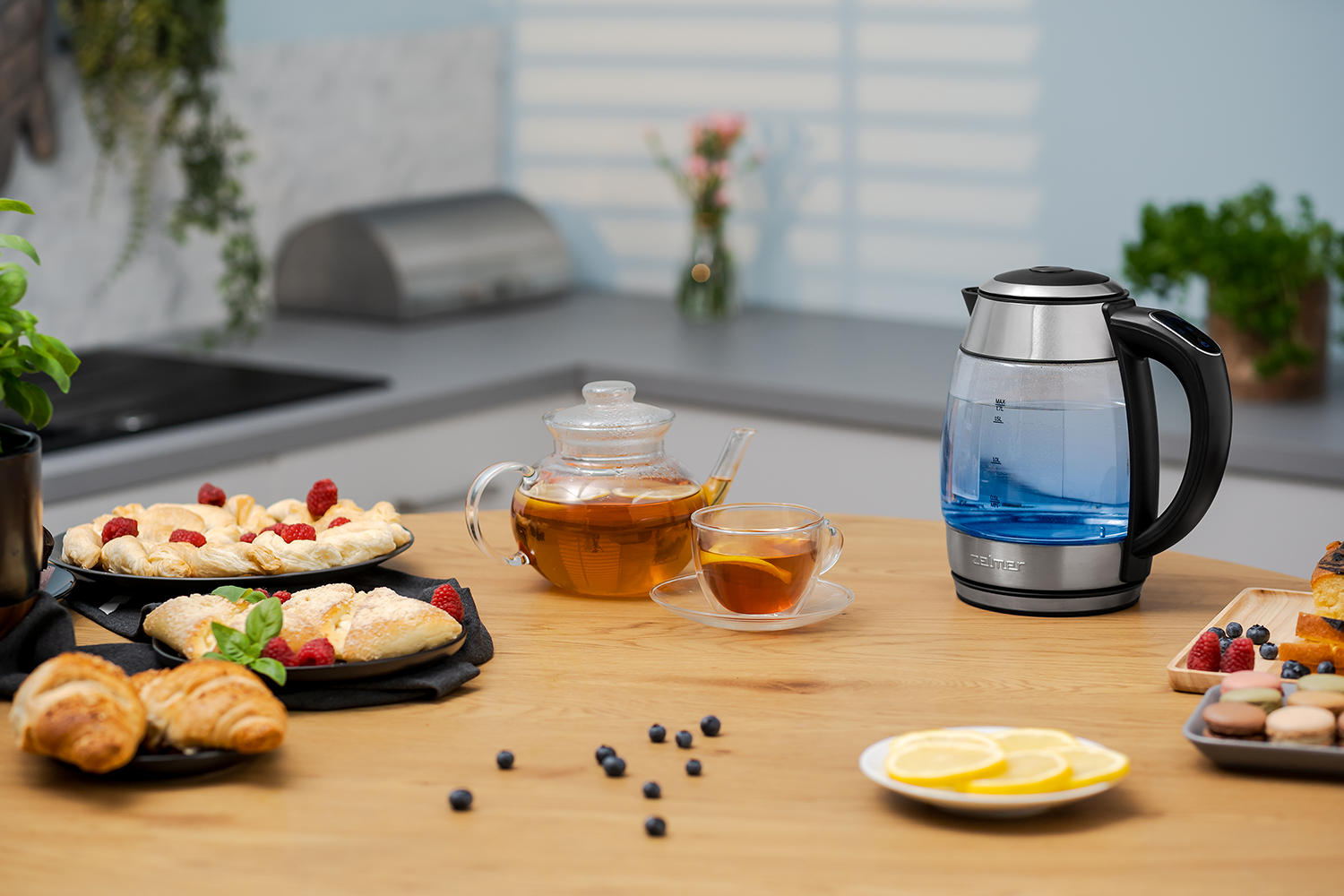 Egy asztal reggeli elemekkel: tea üveg teáskannában, péksütemények, bogyók és egy vízforraló.