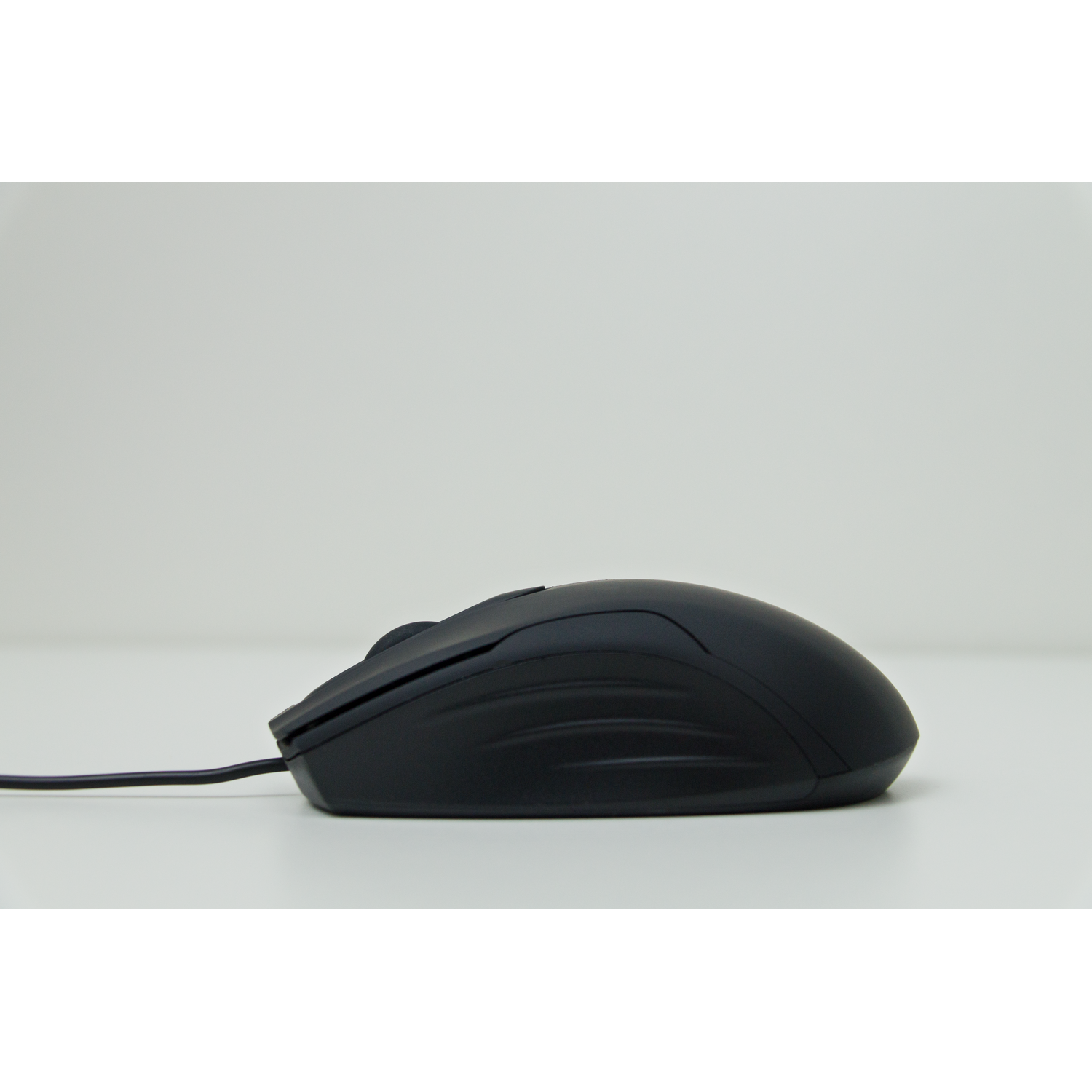 A black computer mouse on a white surface. The mouse is wired and has a simple design.