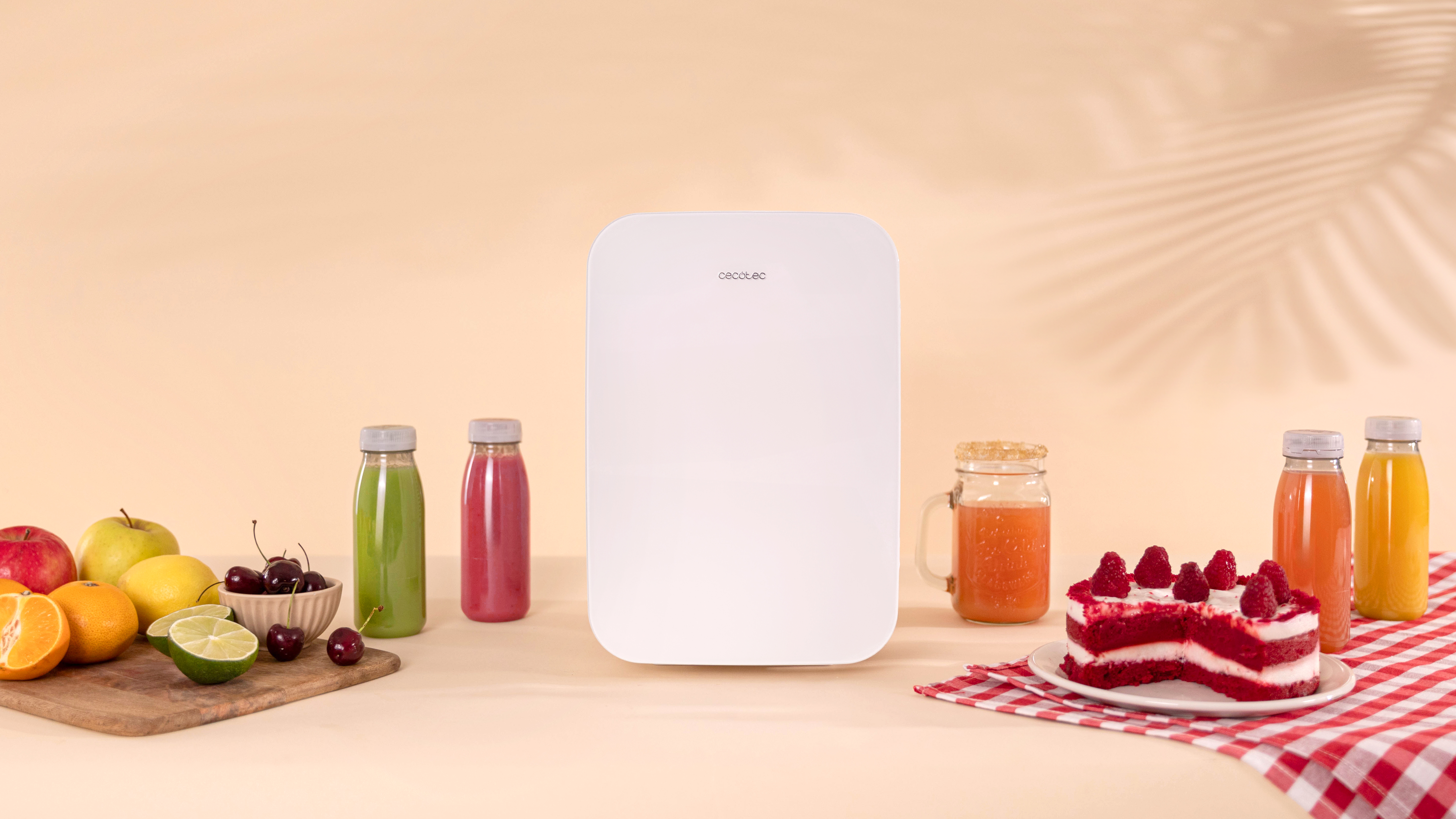 Refrigerador blanco con frutas, pastel y botellas de jugo sobre una superficie beige.