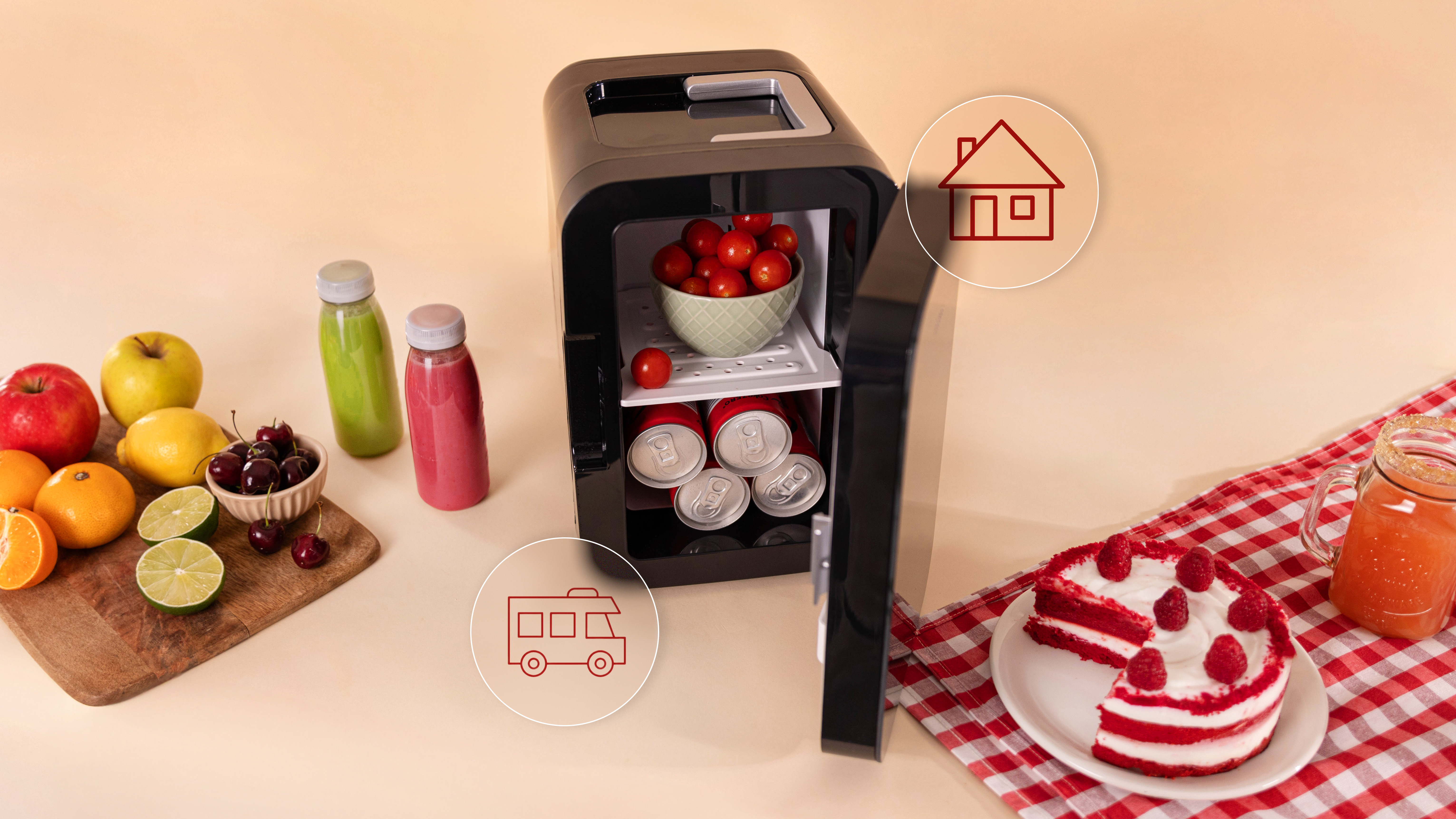Una mini-nevera con bebidas y comida. Abierta, con tarta roja y fruta en mesa cercana.