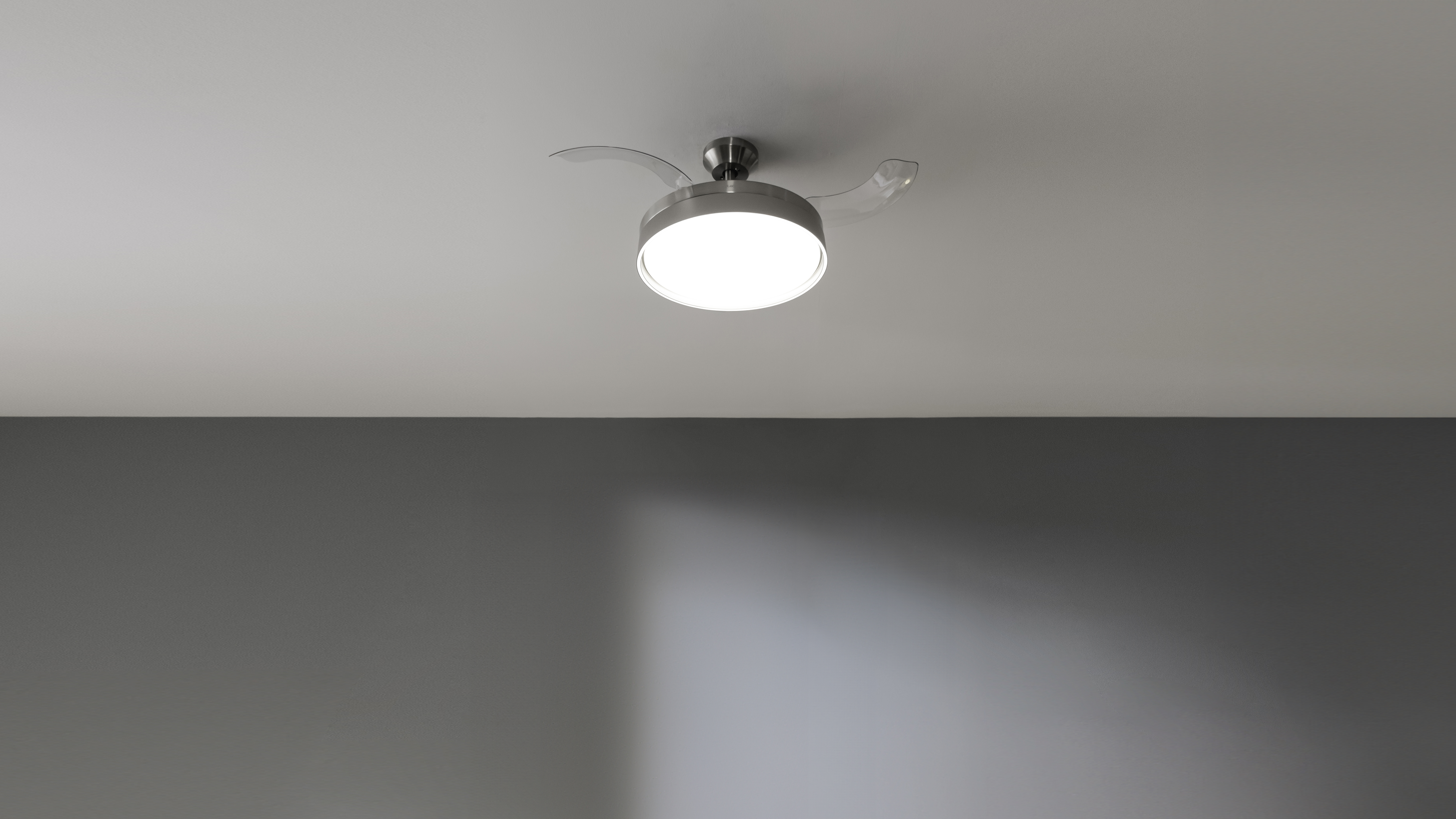 Ventilador de techo con tres aspas y una lámpara. Techo blanco, pared gris.