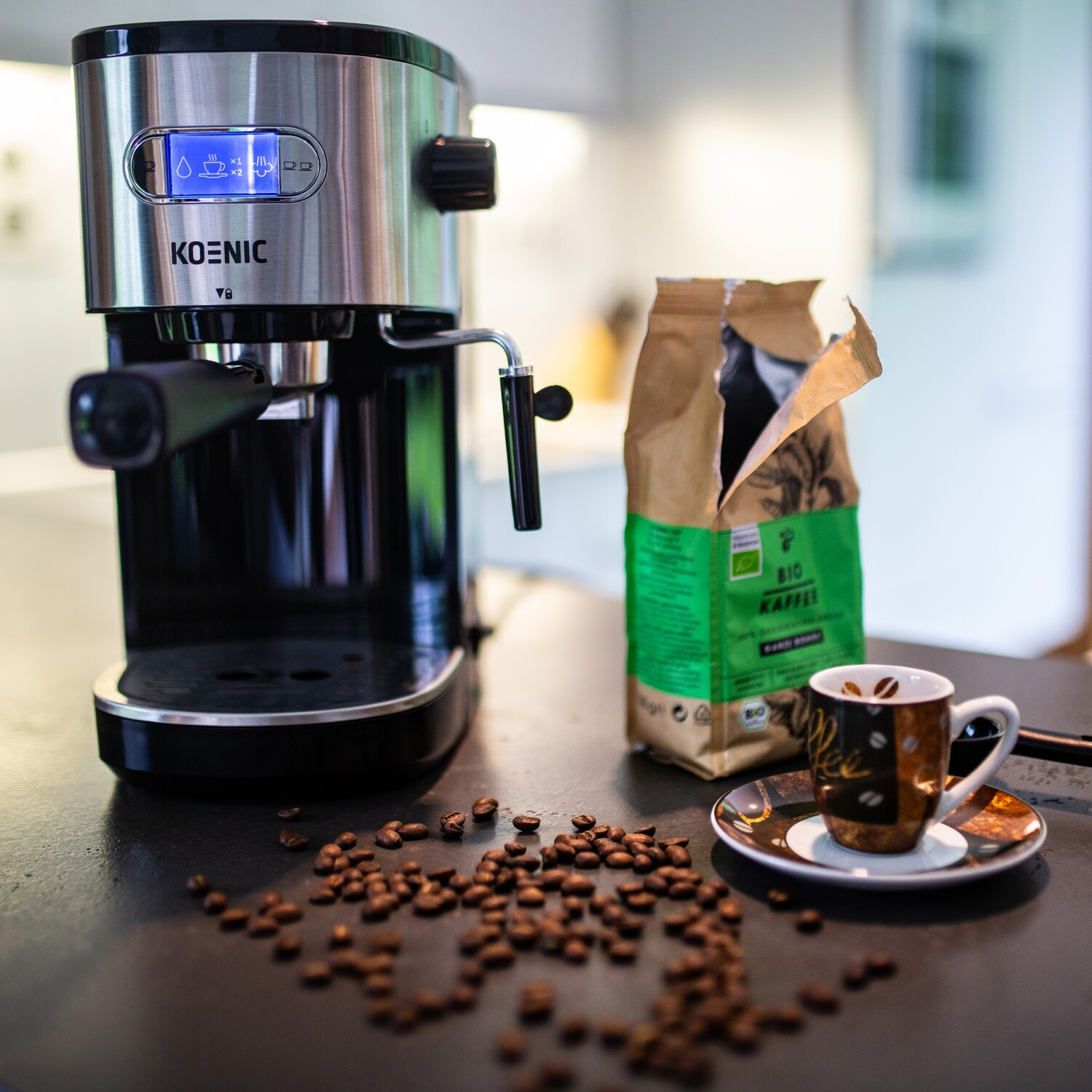 Machine à expresso avec grains de café, une tasse et un sachet de grains de café sur table.