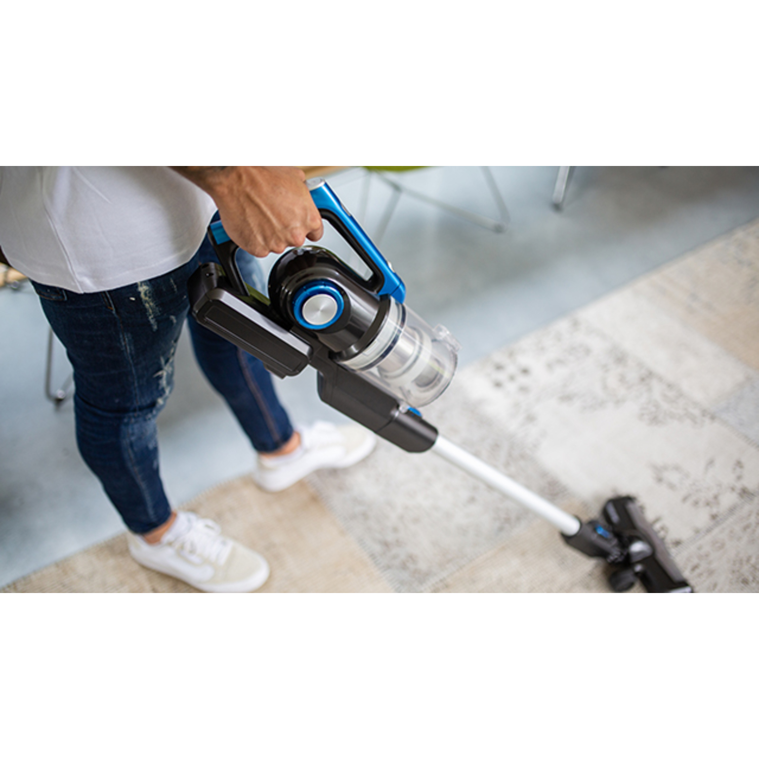 A person vacuuming a patterned carpet with a cordless vacuum cleaner.