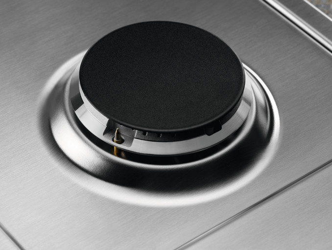 Zbliżenie palnika kuchenki gazowej. Palnik czarny, powierzchnia ze stali nierdzewnej.