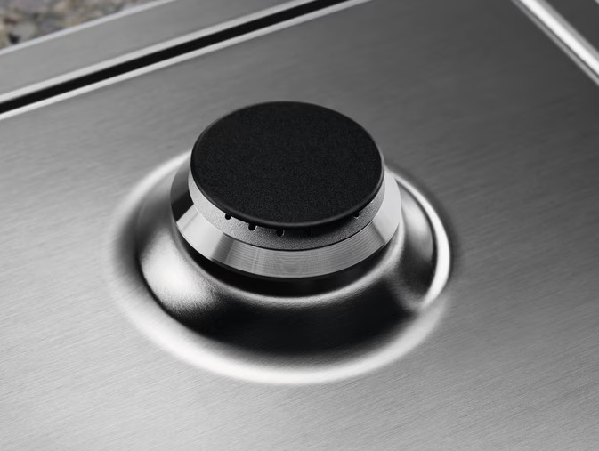 Zbliżenie palnika kuchenki gazowej, powierzchnia ze stali nierdzewnej, z czarnym pokrętłem.