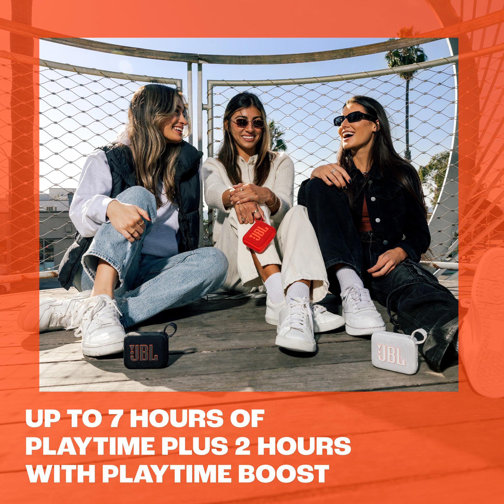 Drei lächelnde Personen mit drei kleinen schwarzen und weißen JBL-Lautsprechern vor sich.