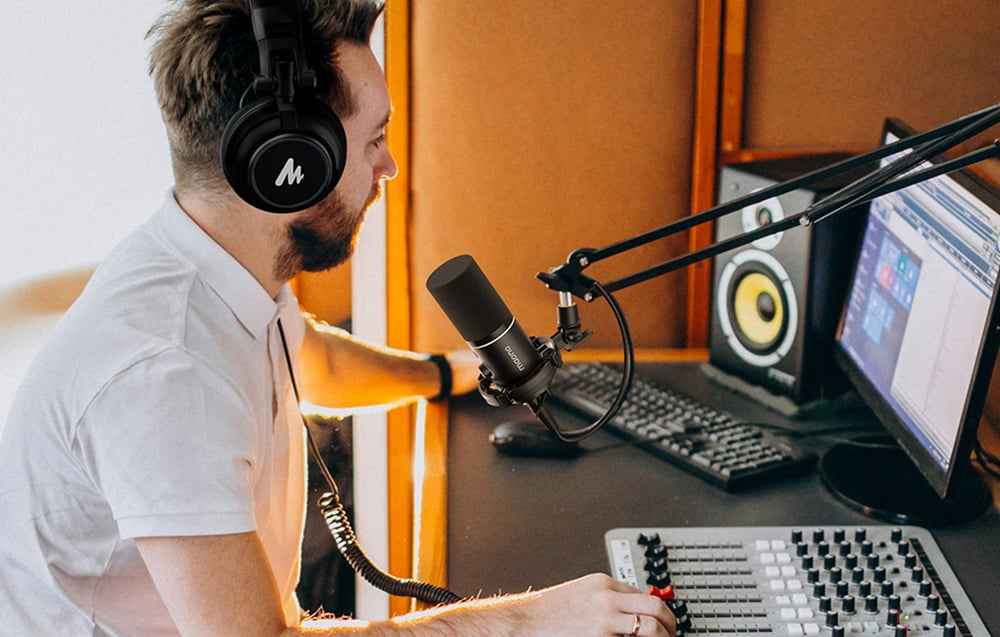 Uomo con cuffie, microfono ed apparecchiature audio. Sfondo studio, scrivania con mixer e computer.