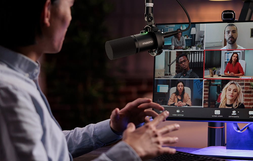 Una persona usa un microfono. Sullo schermo è visualizzata una videoconferenza con più partecipanti.