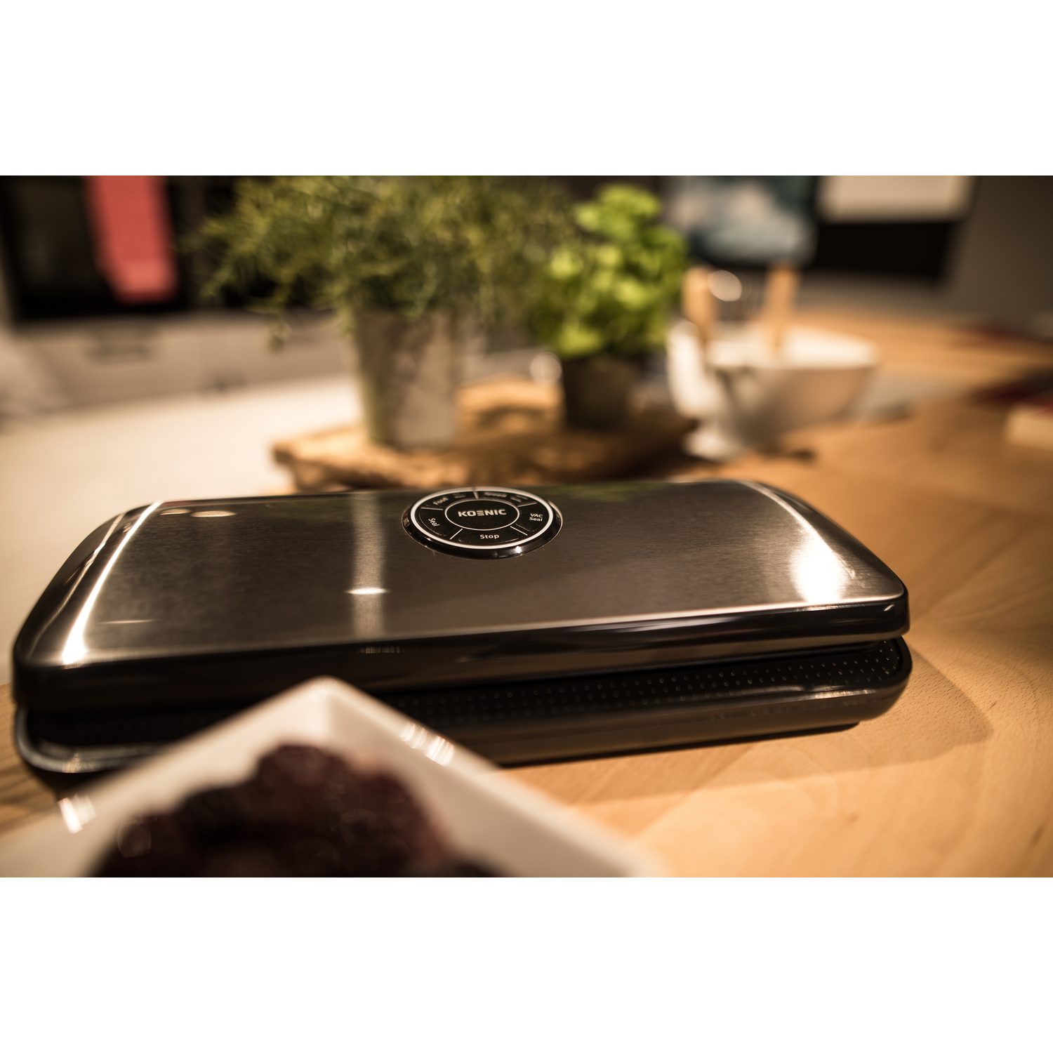 Machine de mise sous vide sur une surface en bois. Dessus en acier inoxydable, base noire.