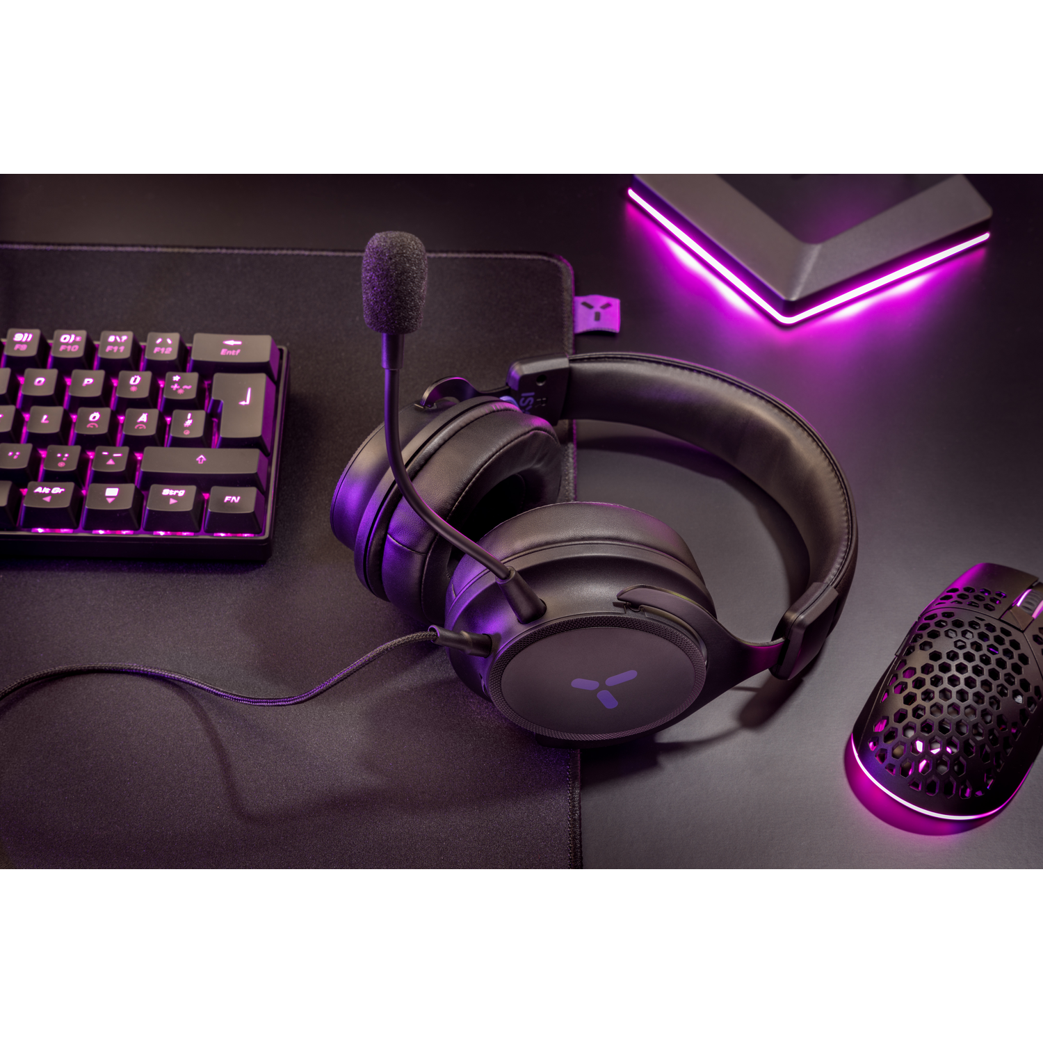 Gaming setup with headphones, mouse, and keyboard. Pink lighting on a black surface.