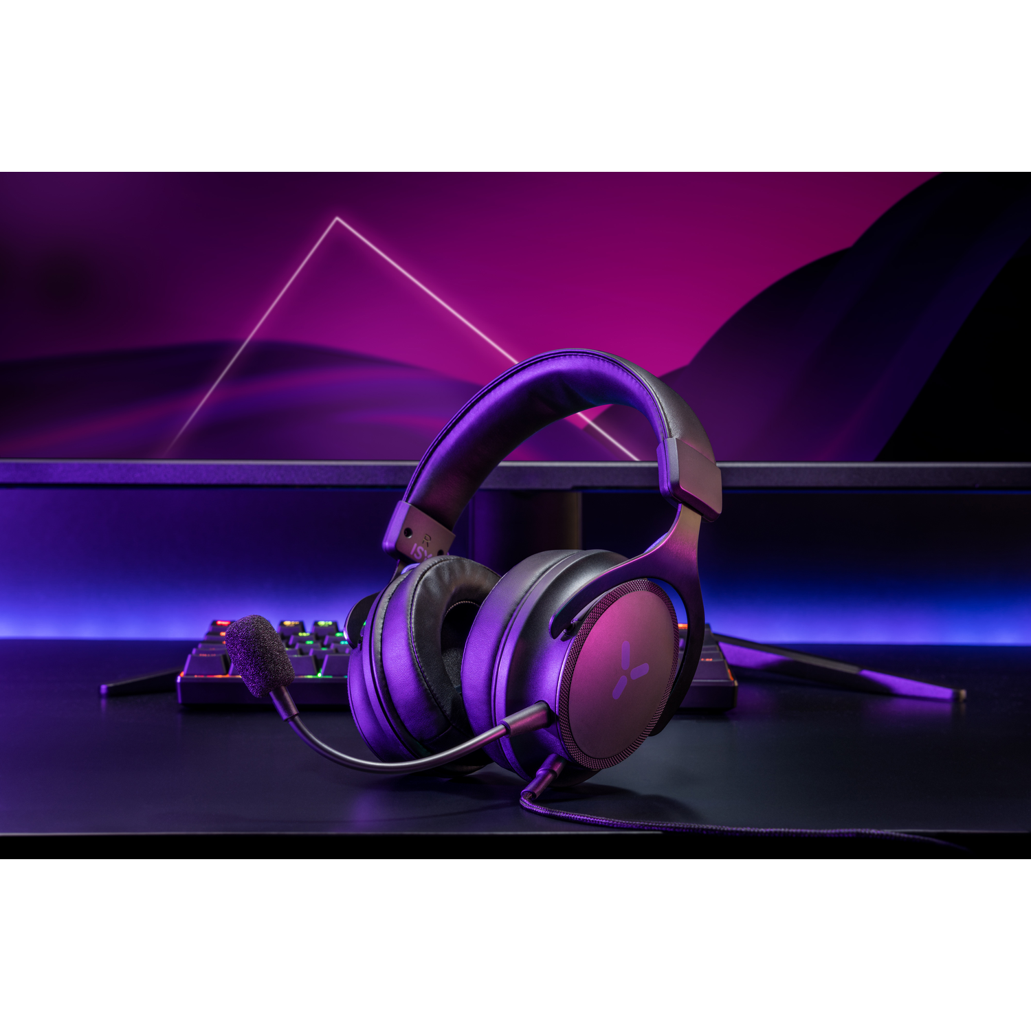 Black and purple gaming headset. It has a microphone and is on a desk with a monitor.