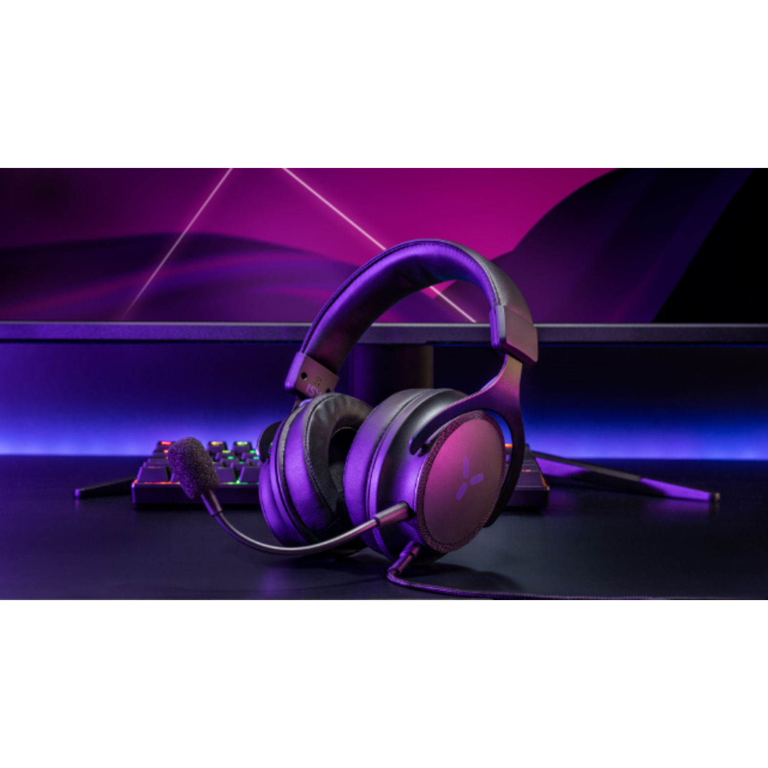 Headphones with microphone on a black desk, with a monitor in the background, lit with purple light.