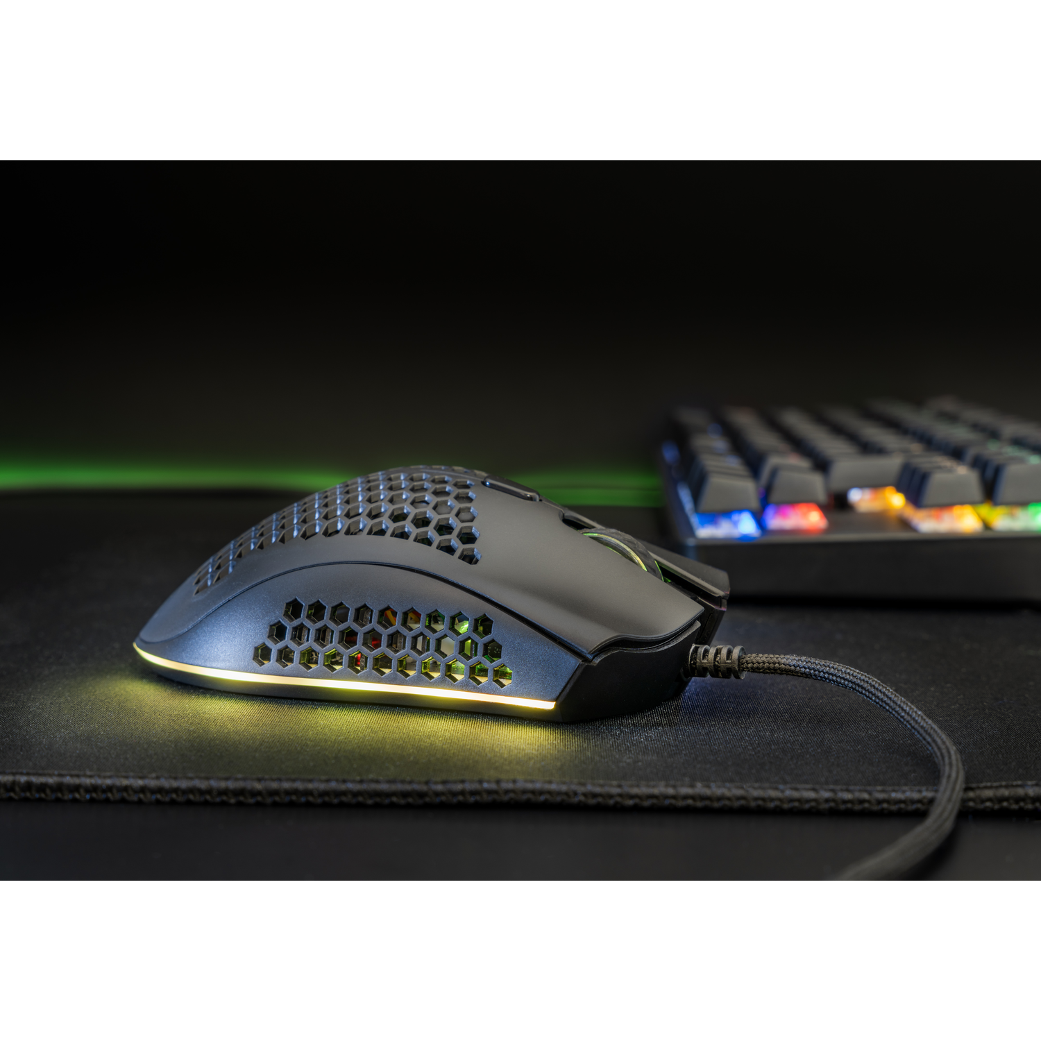 Black gaming mouse on a black mat with a keyboard in the background.