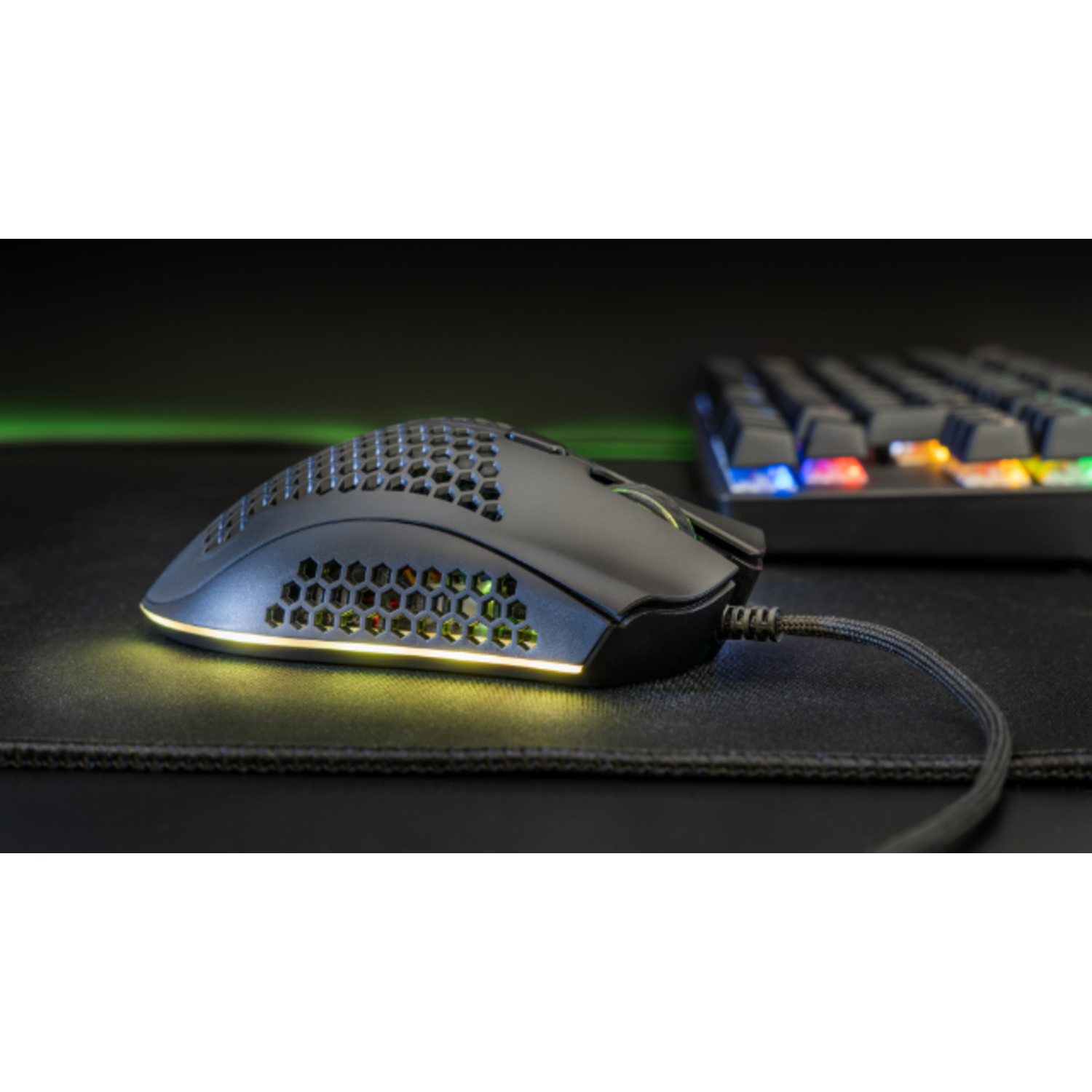Black gaming mouse with RGB lighting on a black mousepad, keyboard in background.
