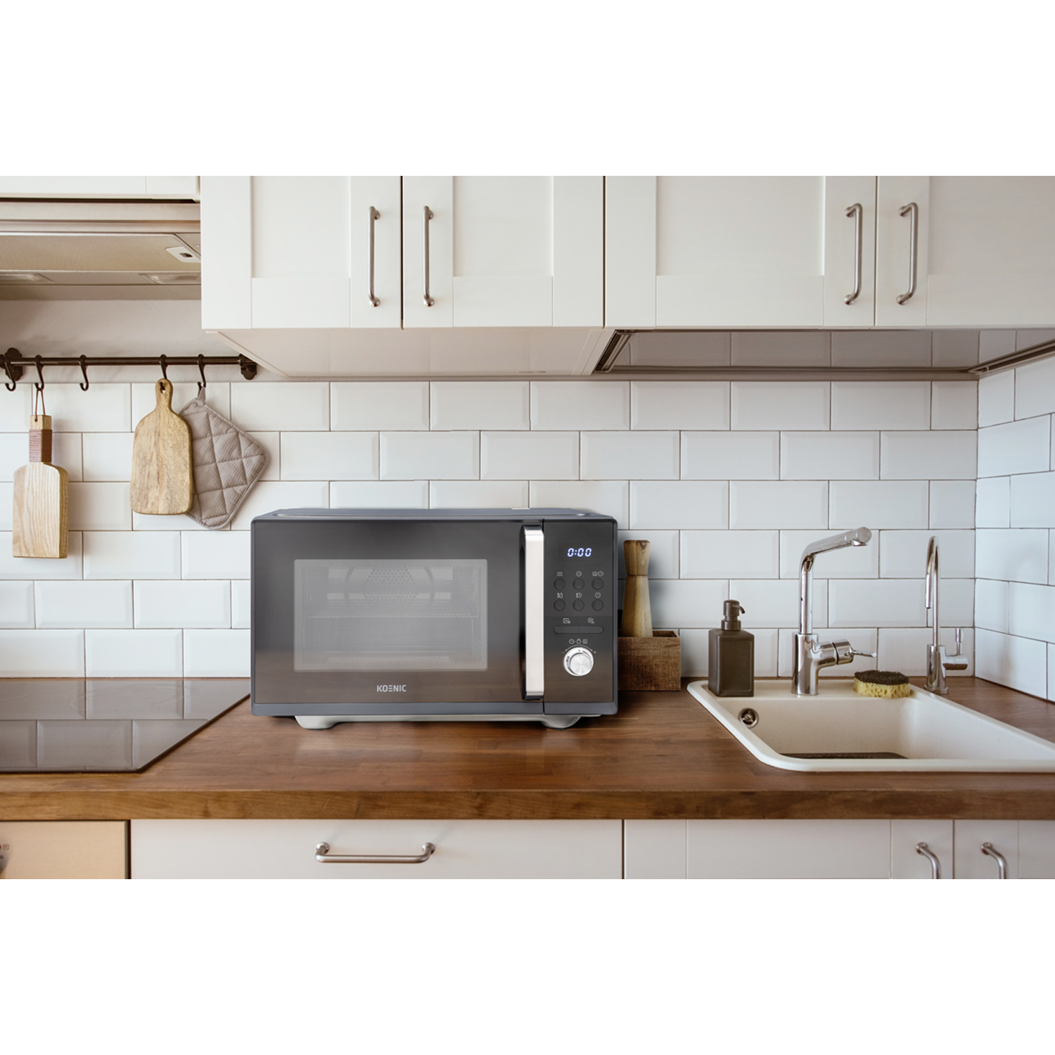 Microwave on wooden countertop. Kitchen setting. White cabinets and tiled wall. Sink and faucet visible.