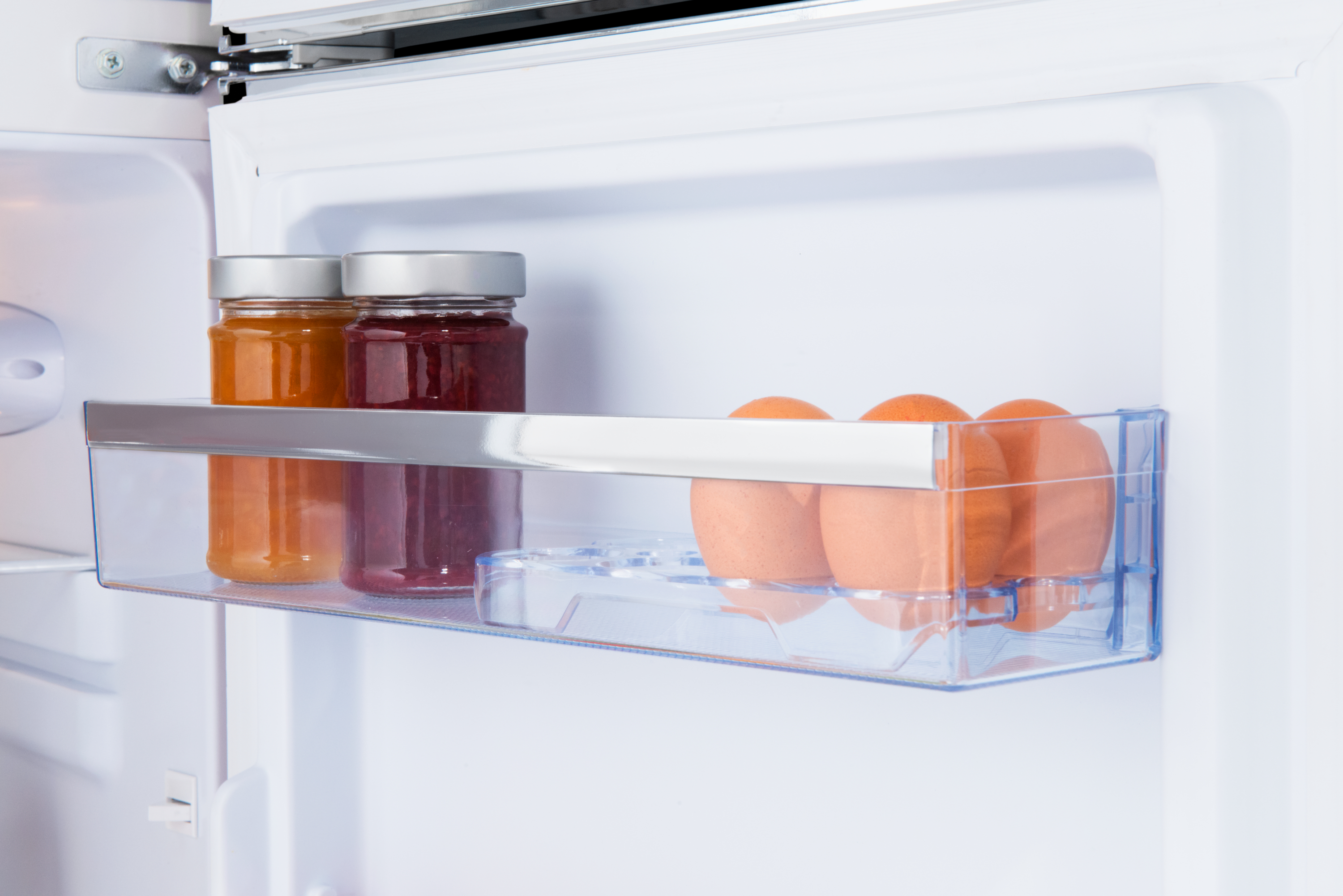 Kühlschrankregal mit Marmeladengläsern und Eiern in einem transparenten Behälter.
