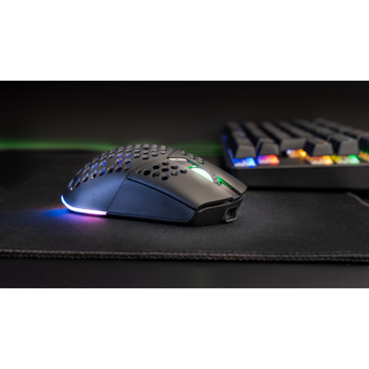 A black gaming mouse with a glowing light. A keyboard is in the background on a black mousepad.