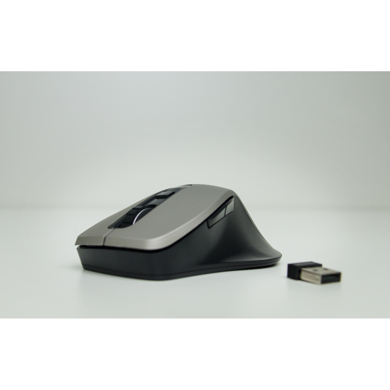 A gray and black computer mouse with a USB receiver on a white surface.