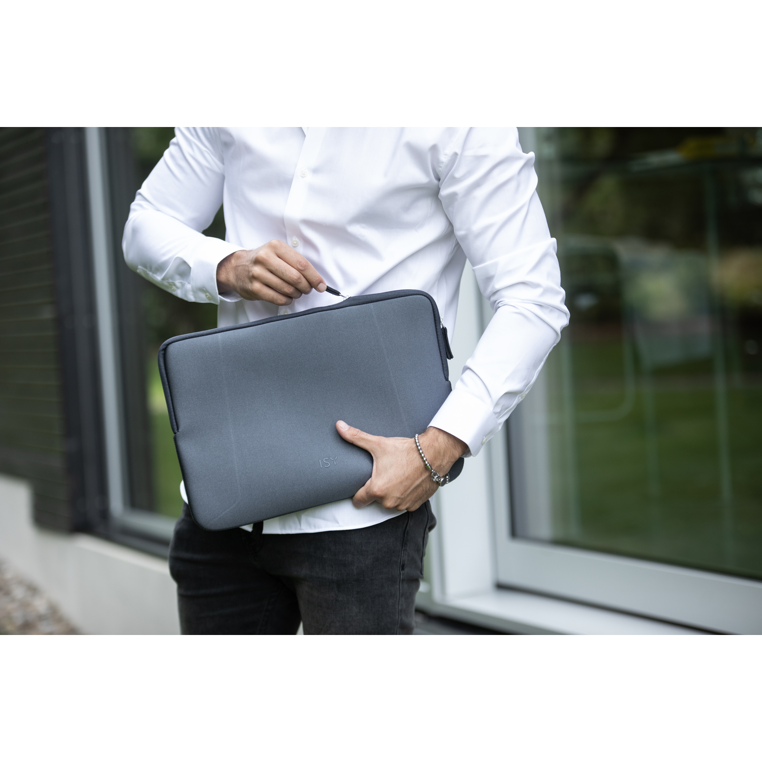 A man in a white shirt holds a gray laptop sleeve. The sleeve has a zipper.