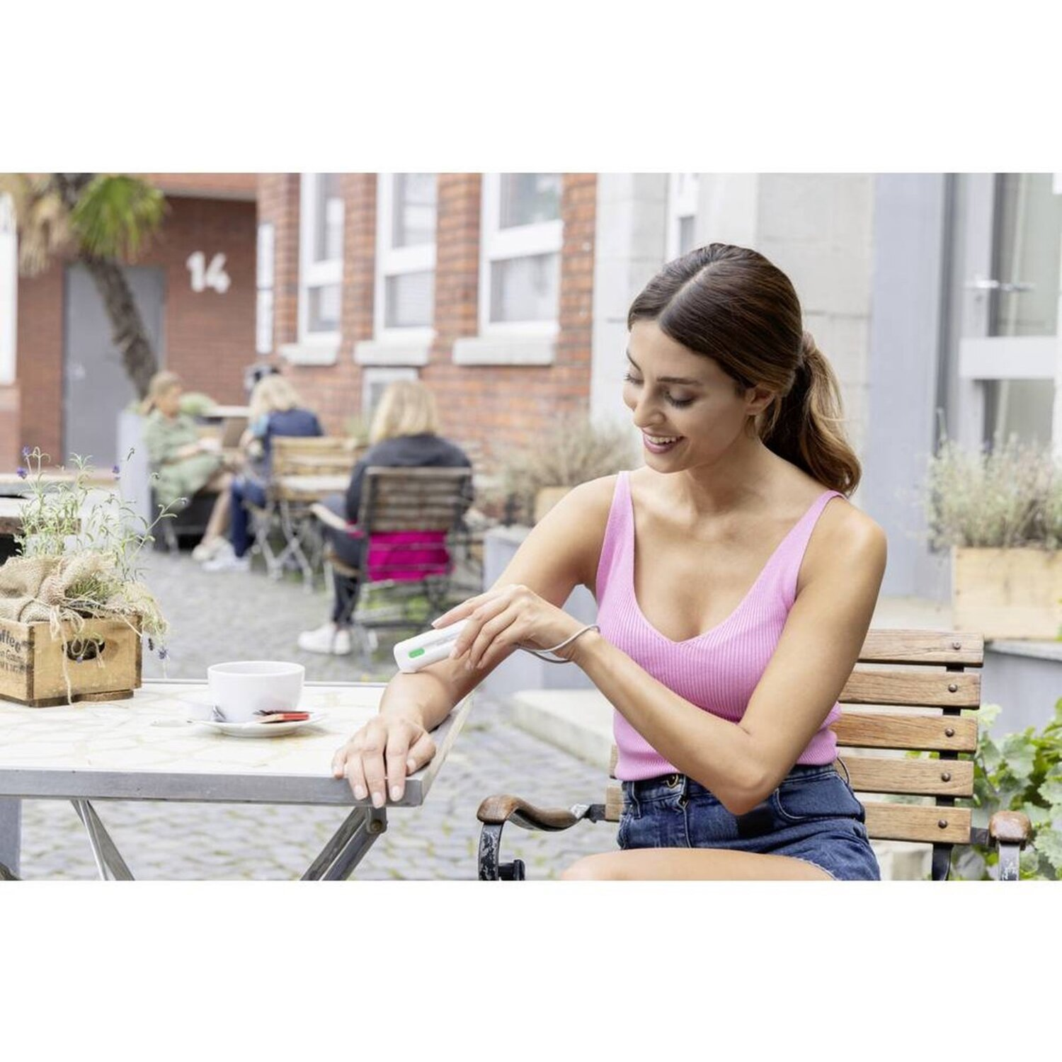 Woman applies device to arm while sitting at table outside.