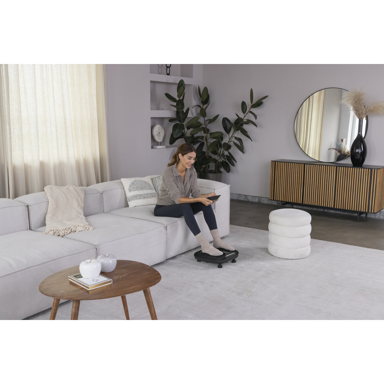 Woman sitting on a white sofa using a tablet.  A foot massager is in use.