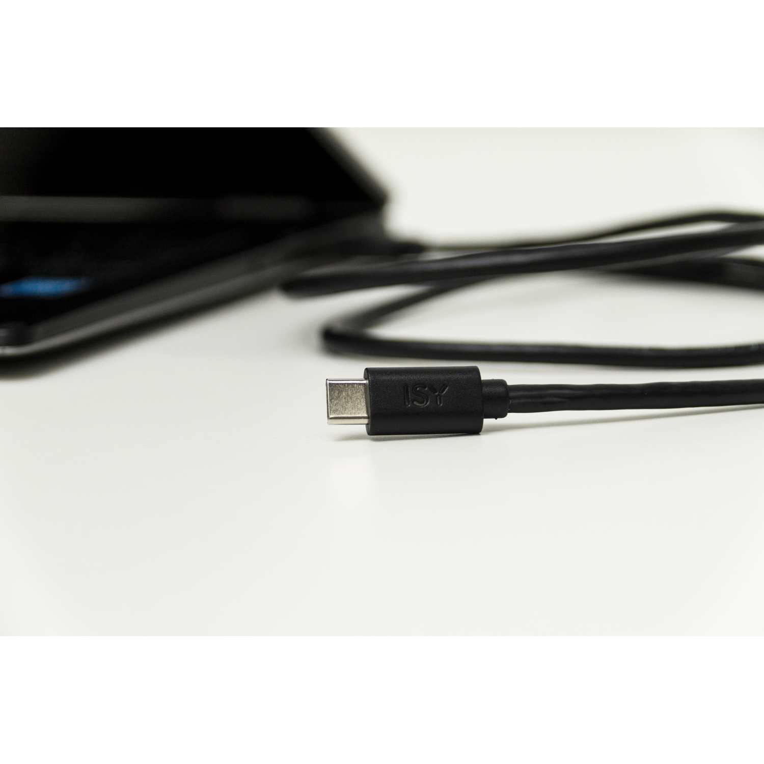 USB-C cable with connector. Black cable on a white surface. Black device in the blurred background.
