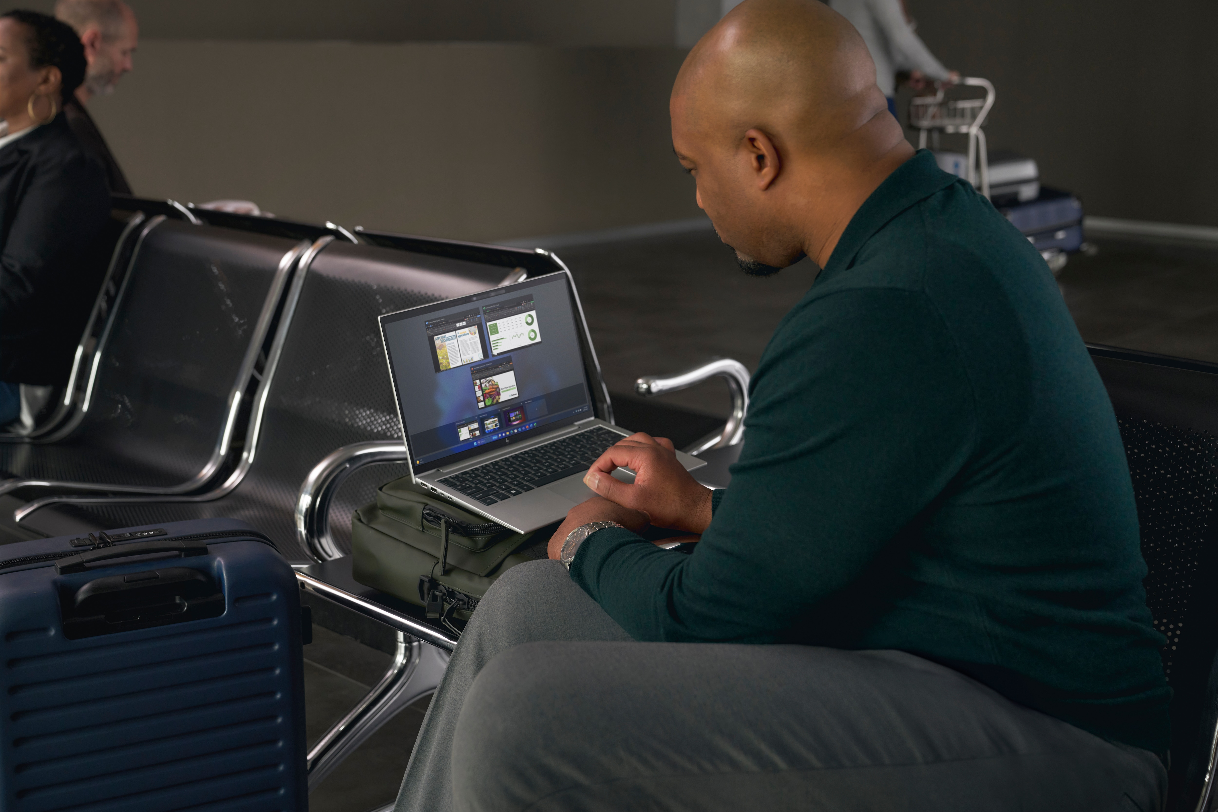 Ein Mann arbeitet am Flughafen an einem Laptop. Ein Koffer steht neben ihm.