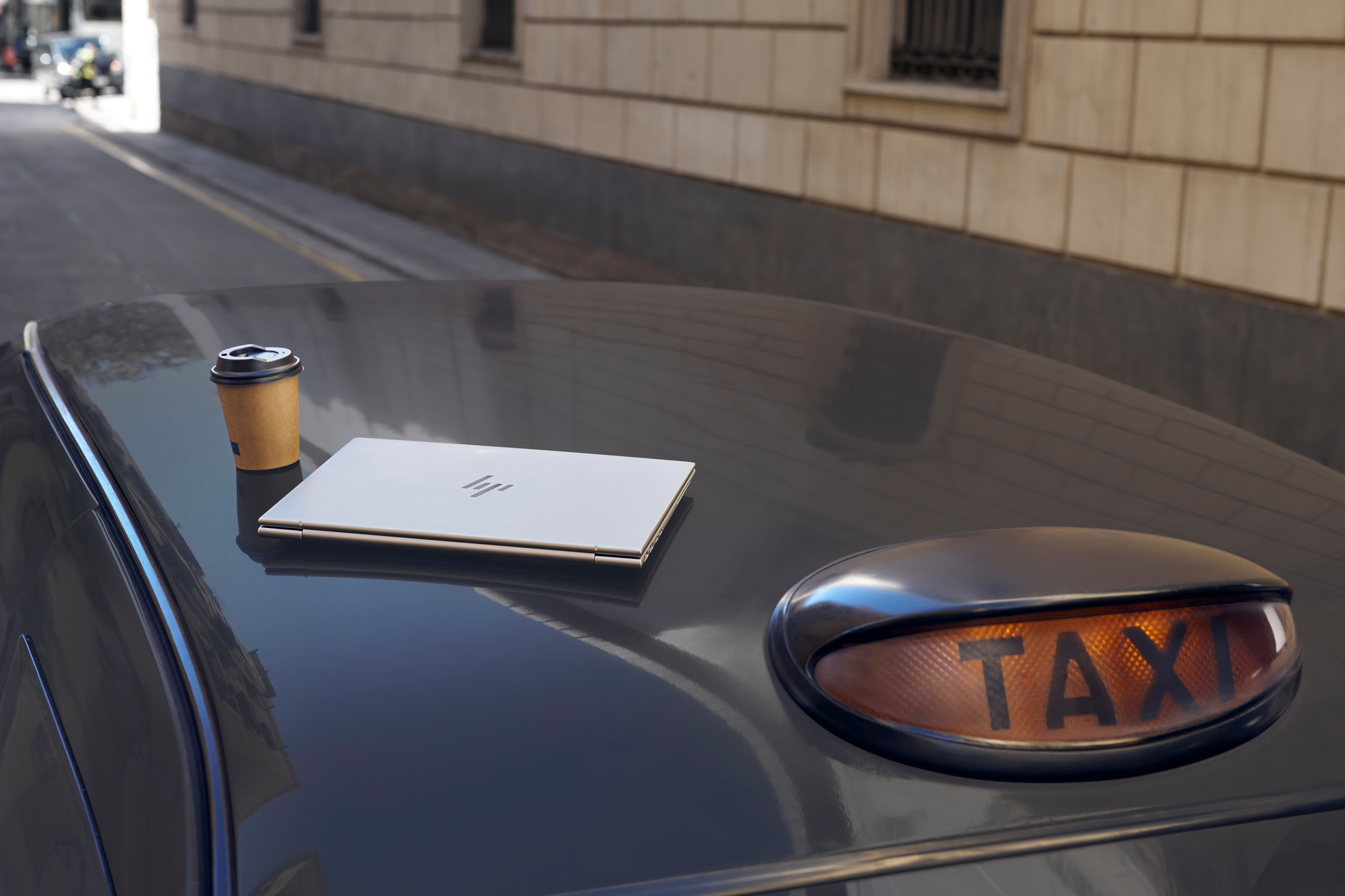 Laptop und Kaffeetasse auf einem Taxidach, im Hintergrund ein TAXI-Schild.