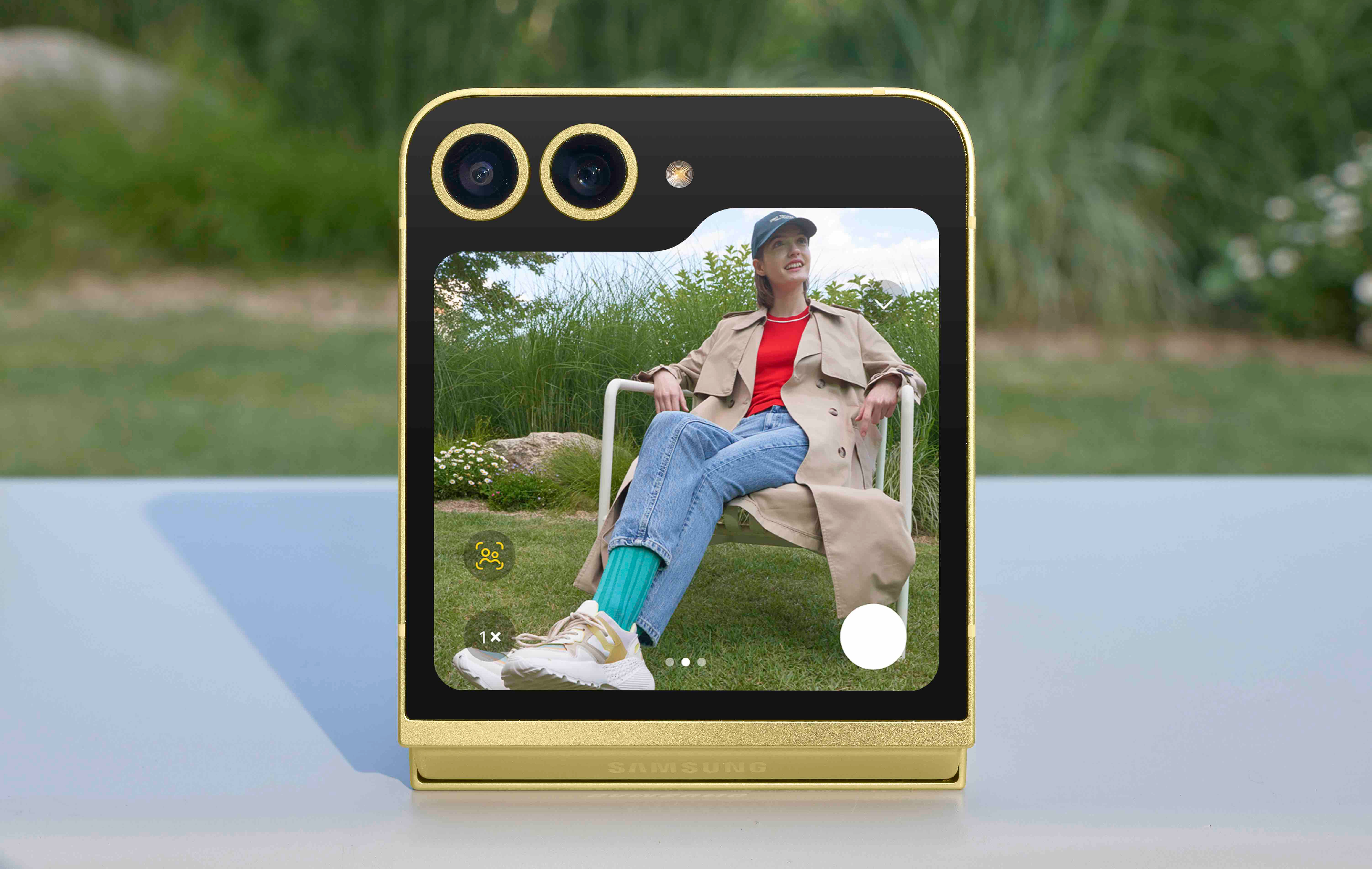 Złoty składany telefon Samsung otwarty, pokazujący kobietę robiącą zdjęcie na zewnątrz.