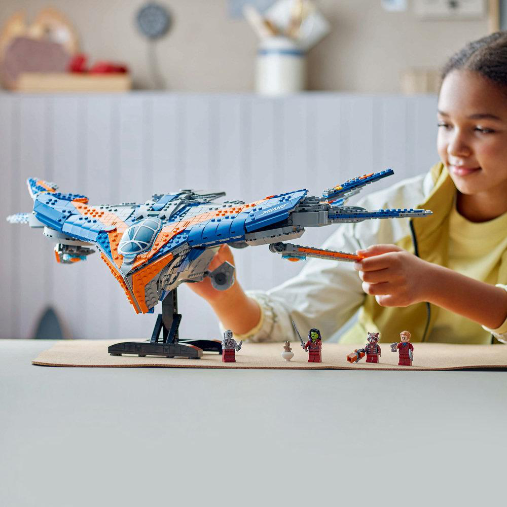 Ein Mädchen hält ein blaues und orangefarbenes Lego-Raumschiff mit Figuren davor.