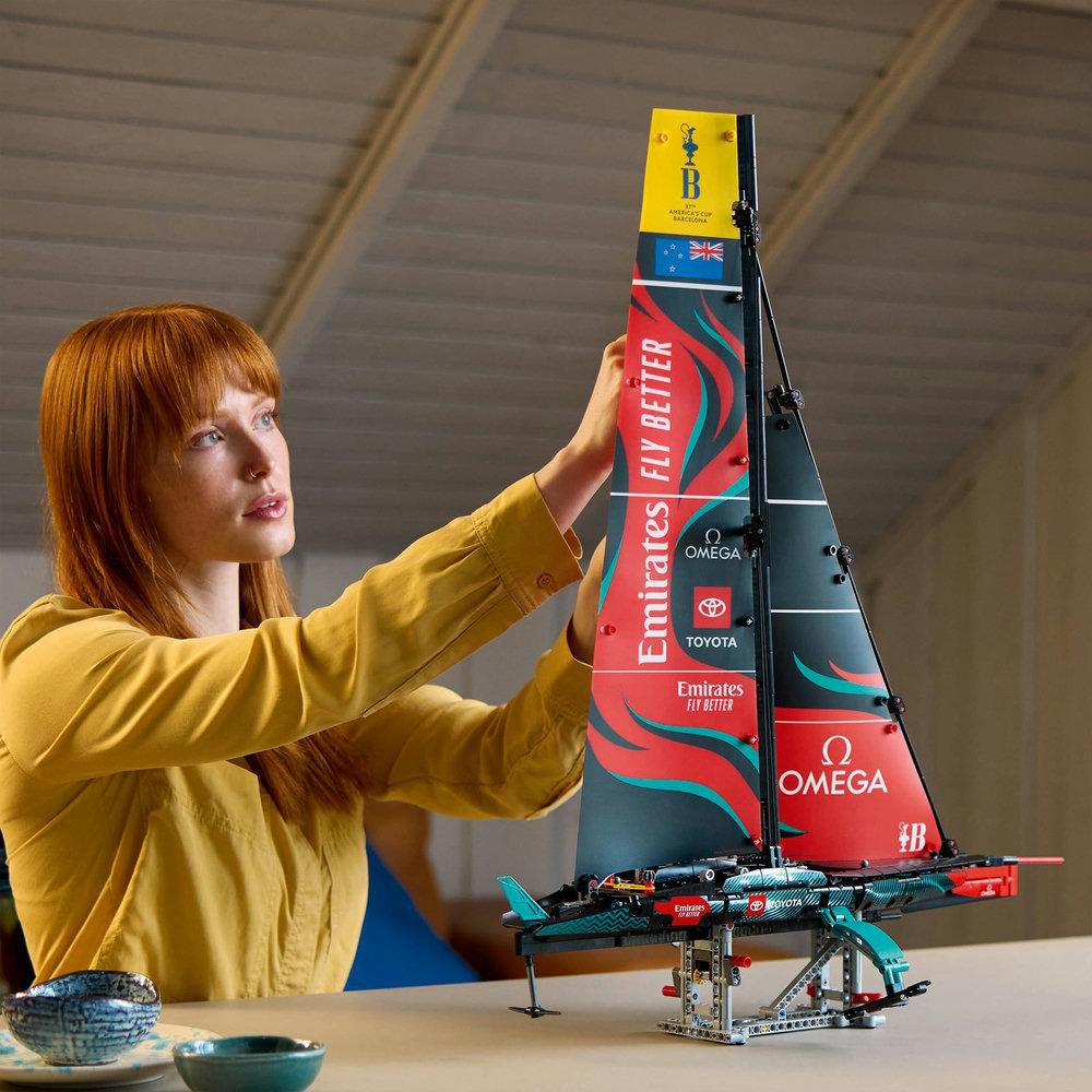 Frau, die ein Modellsegelboot zusammenbaut. Segel mit Logos. Holztisch. Blaue und grüne Schalen.