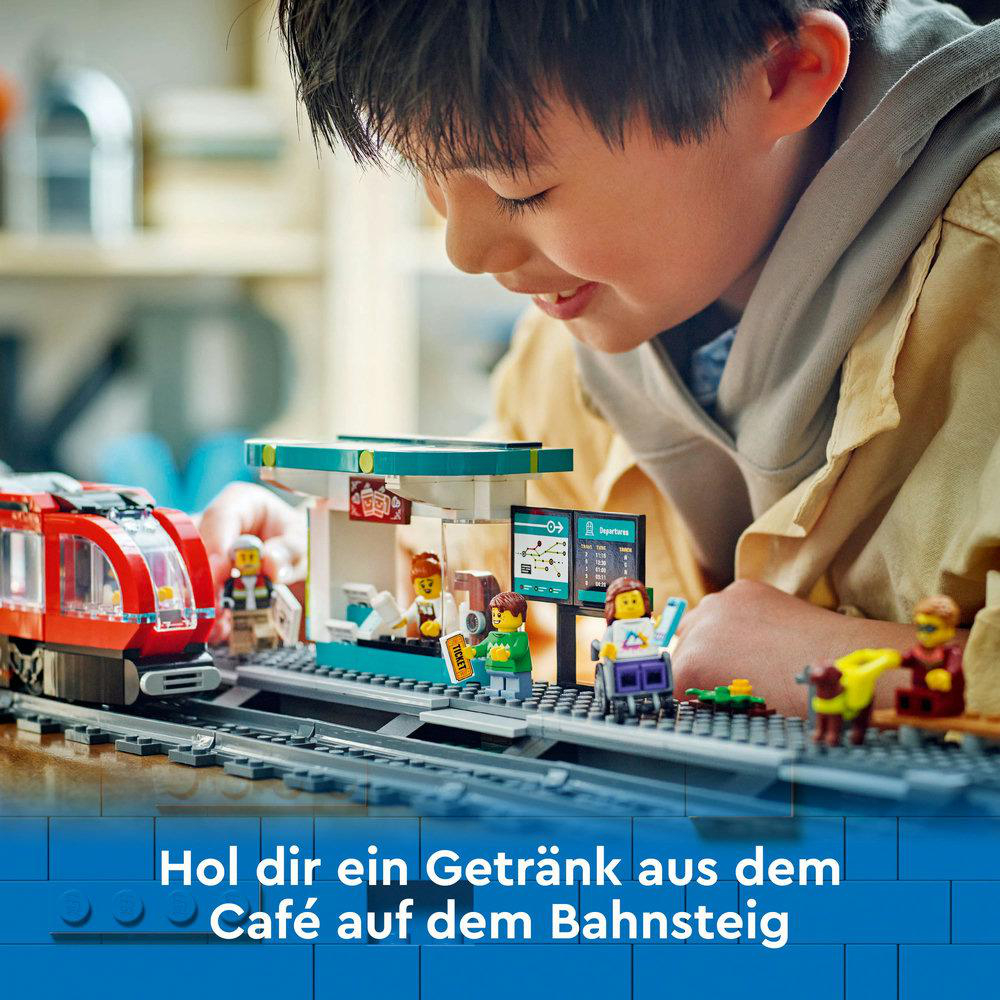 Ein Junge spielt mit einem LEGO-Zug-Set. Ein roter Zug steht auf Gleisen neben einem Bahnhof.