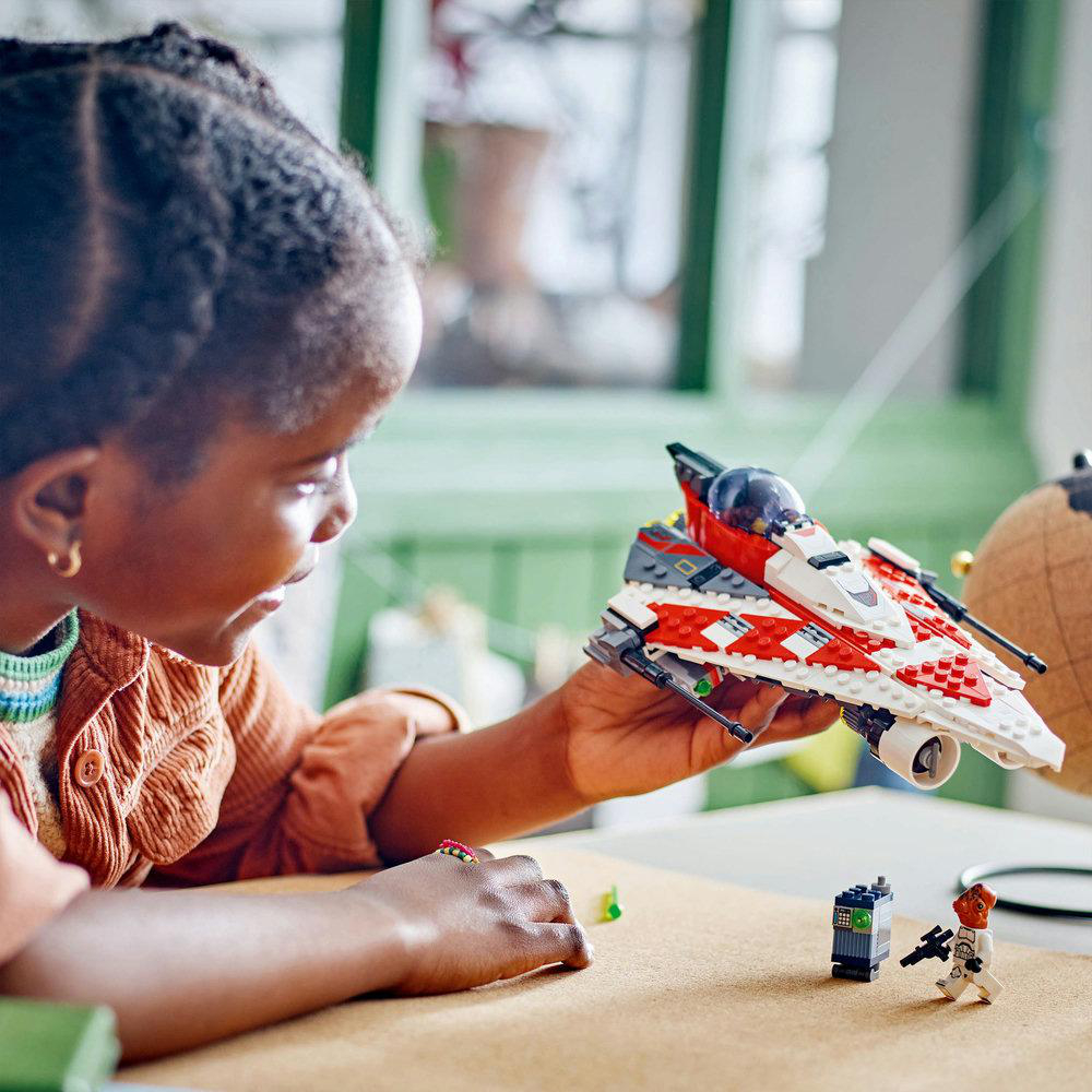 Ein Kind, das ein Lego-Raumschiff hält, mit Lego-Figuren und anderen Blöcken auf einem Tisch.