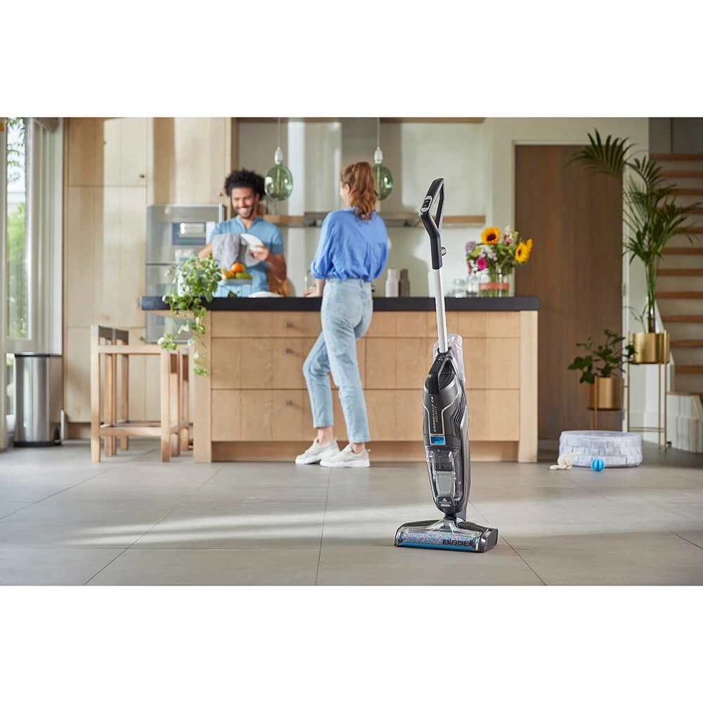 Una mujer y un hombre en una cocina, con una aspiradora en primer plano.