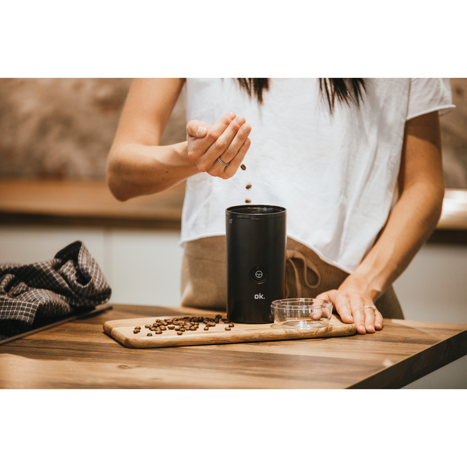 A woman pouring coffee beans from her hand into a black coffee grinder on a wooden board.
